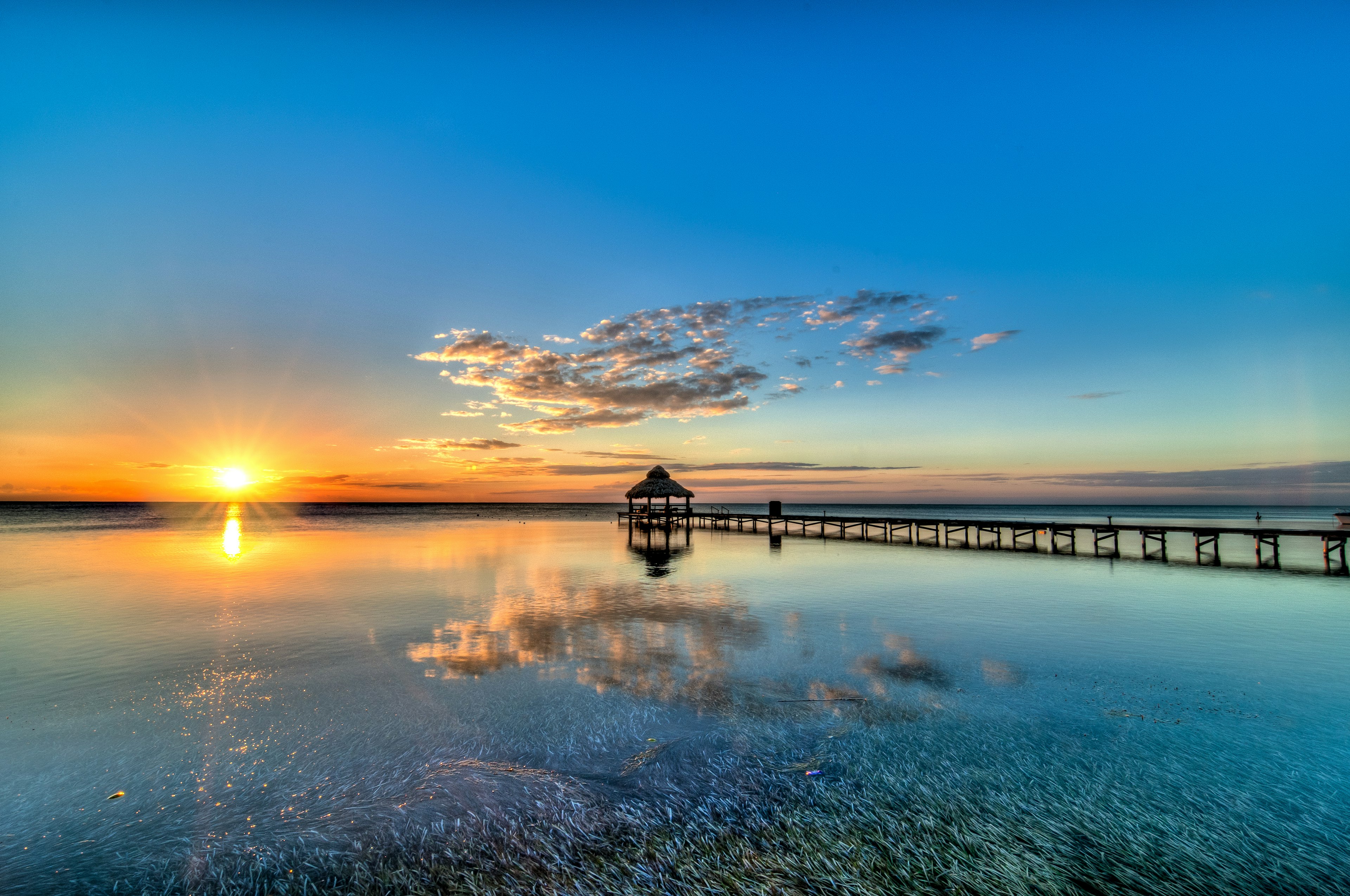 An orange sunset streaks the sky over the ocean with a pier appearing as a silhouette