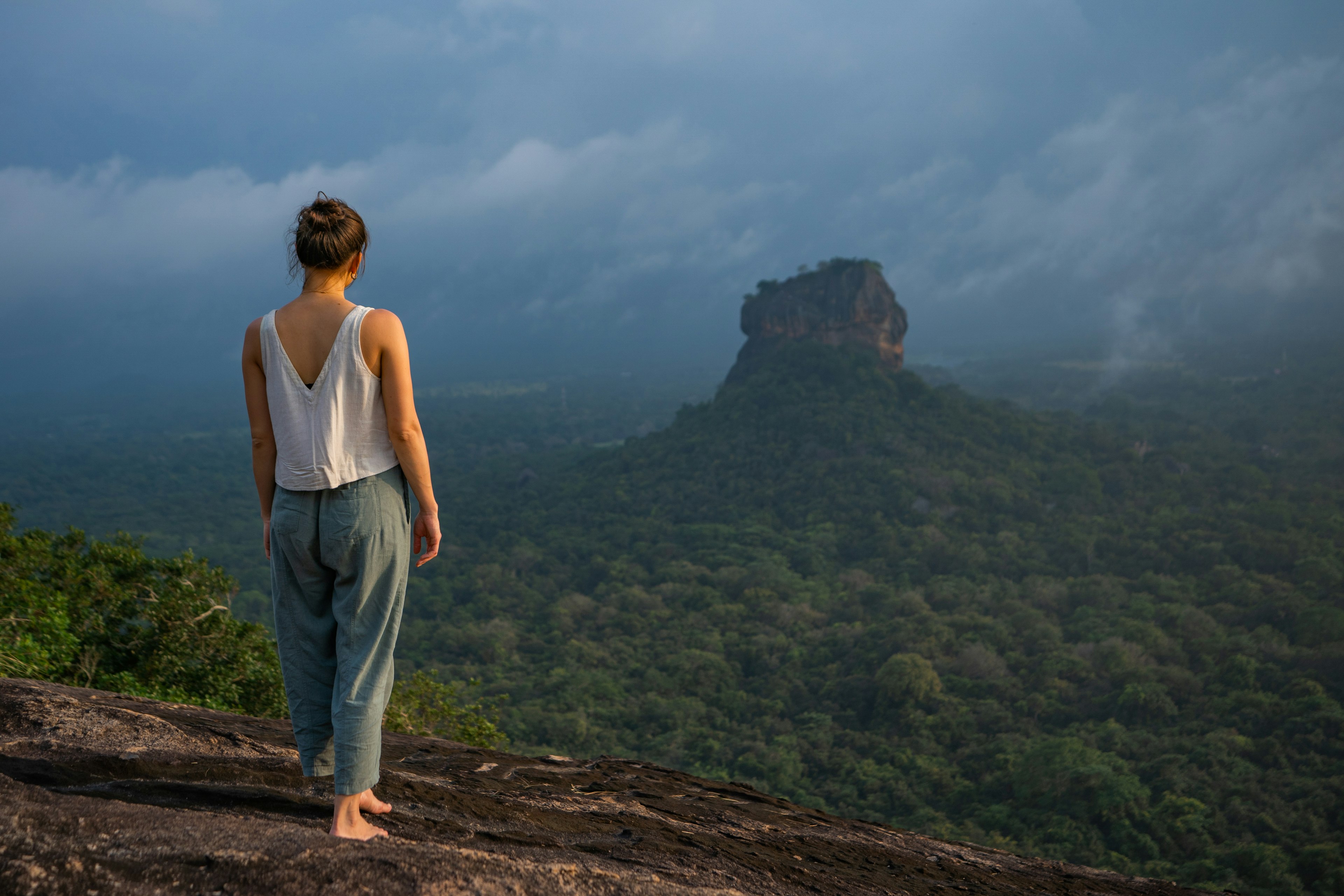 A woman in loose clothing admires a hazy view of a rocky outcrop at sunrise