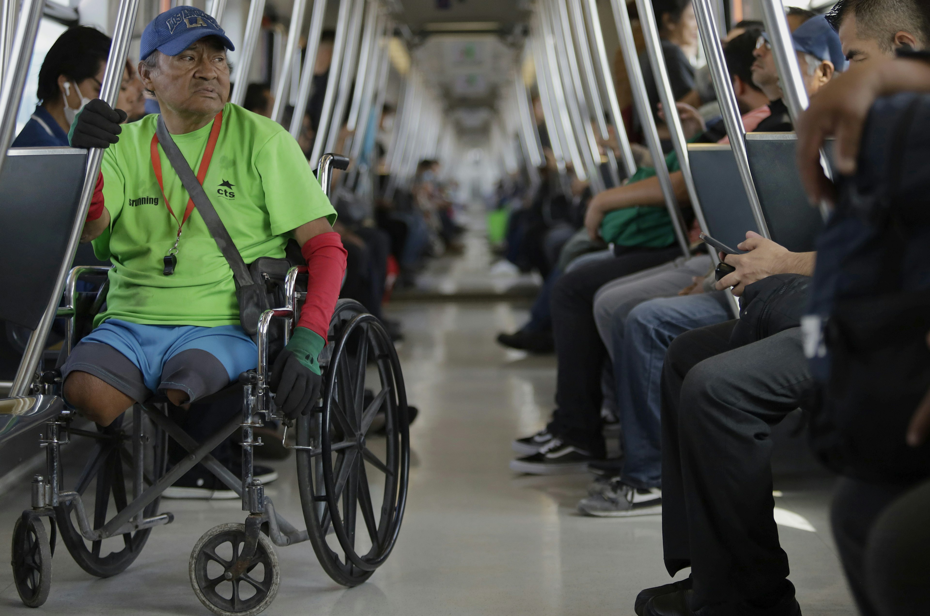 A person in a wheelchair inside a crowded subway car. Seated passengers are visible in the background.