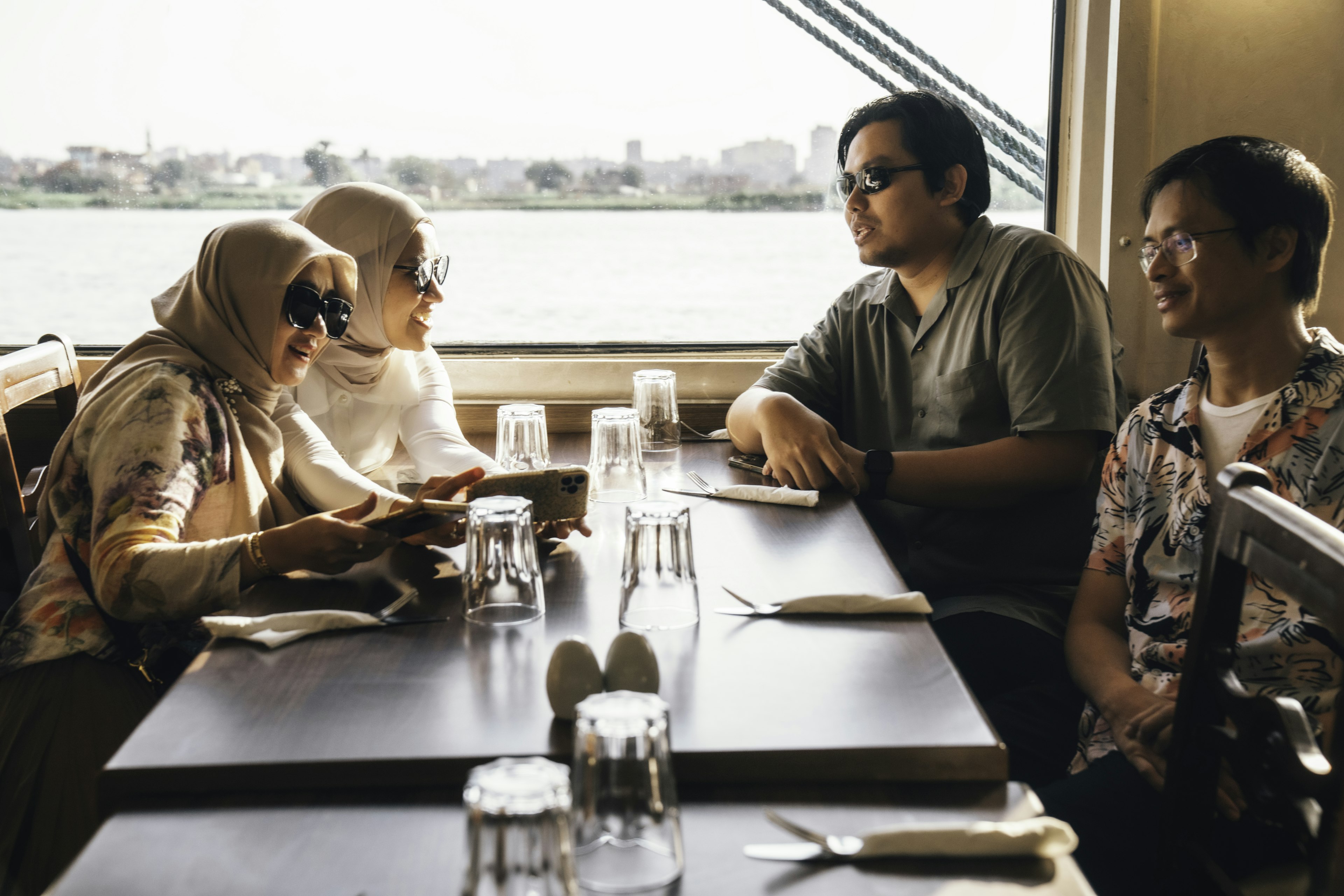 Группа из четырех друзей на речном круизе смотрят на что-то вместе на мобильном телефоне