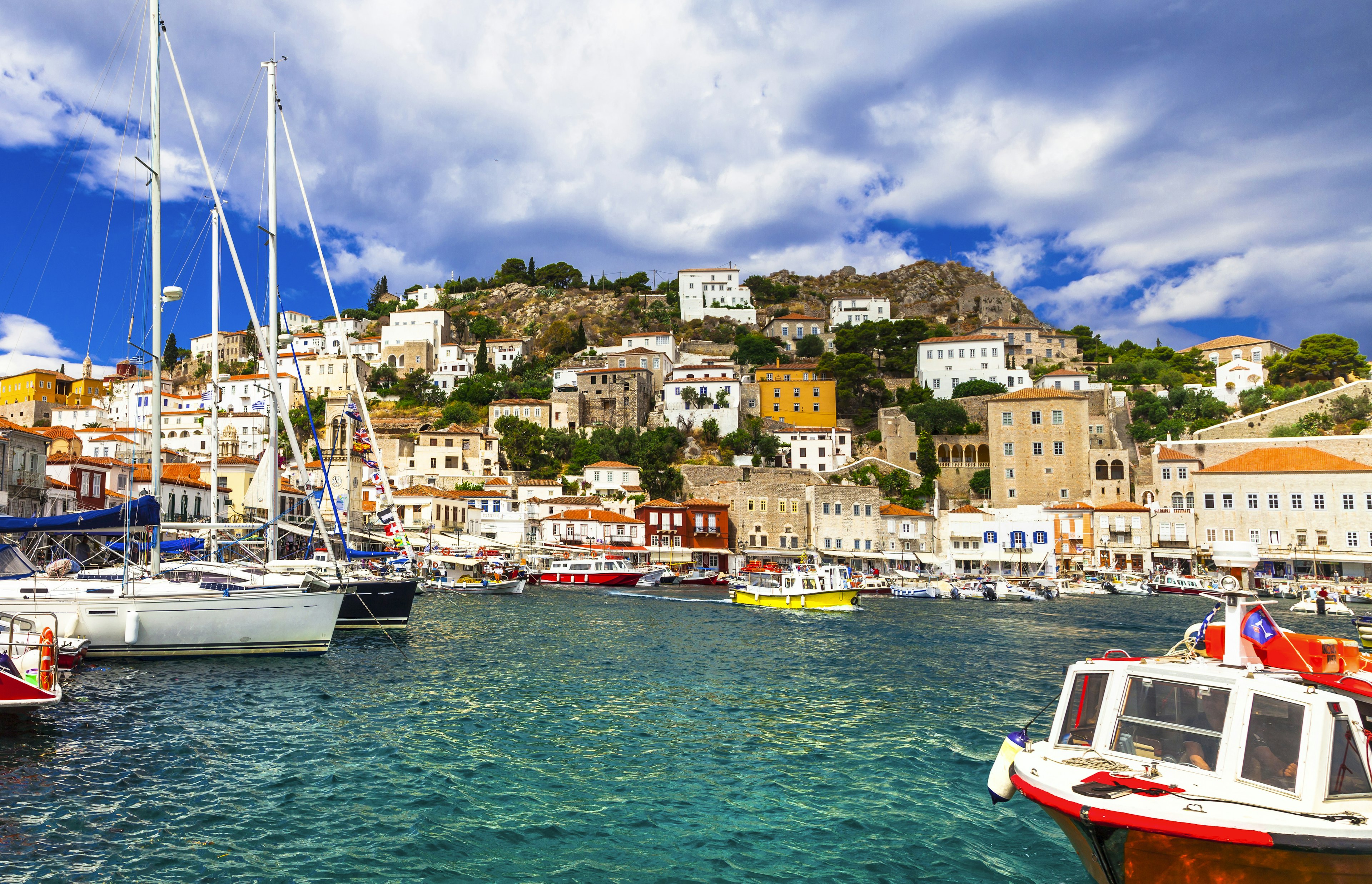 Fishing boats in the harbour at Hydra, with the town's houses huddled on a hillside behind them.