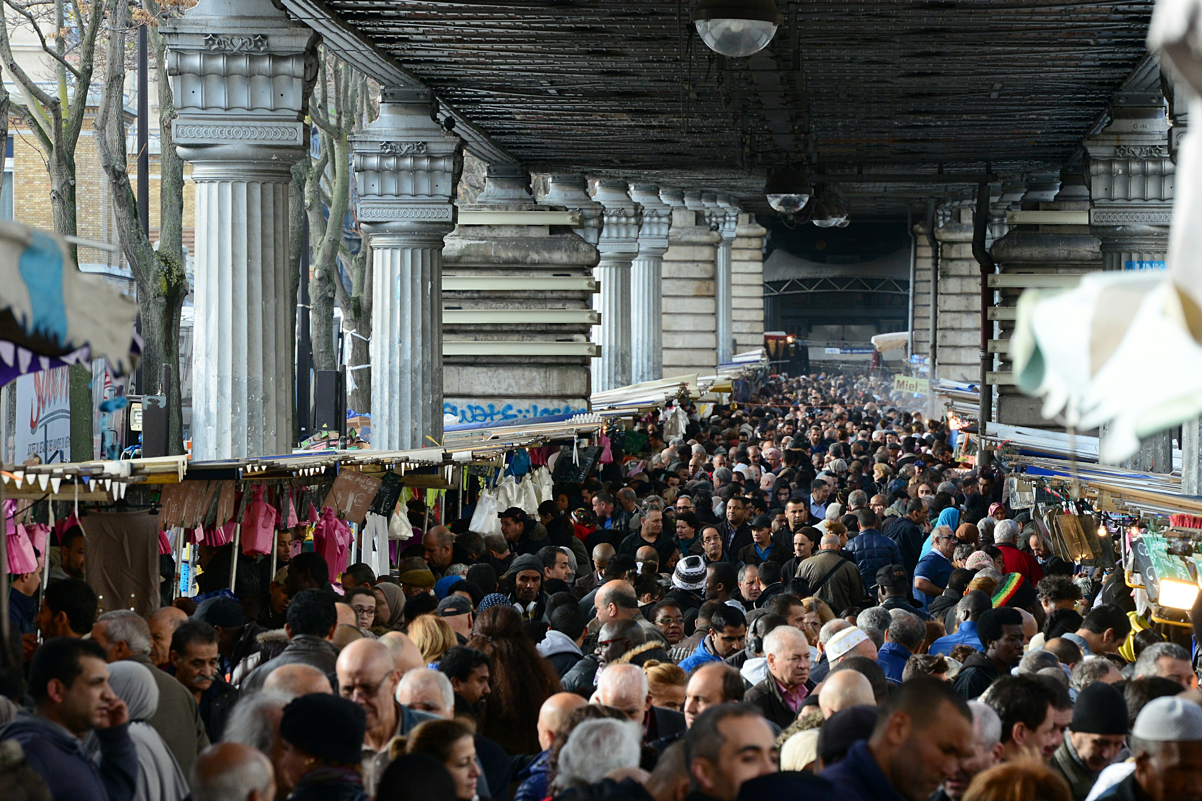 Thousands of people crowd by stalls at a market underneath a train viaduct in Paris, France