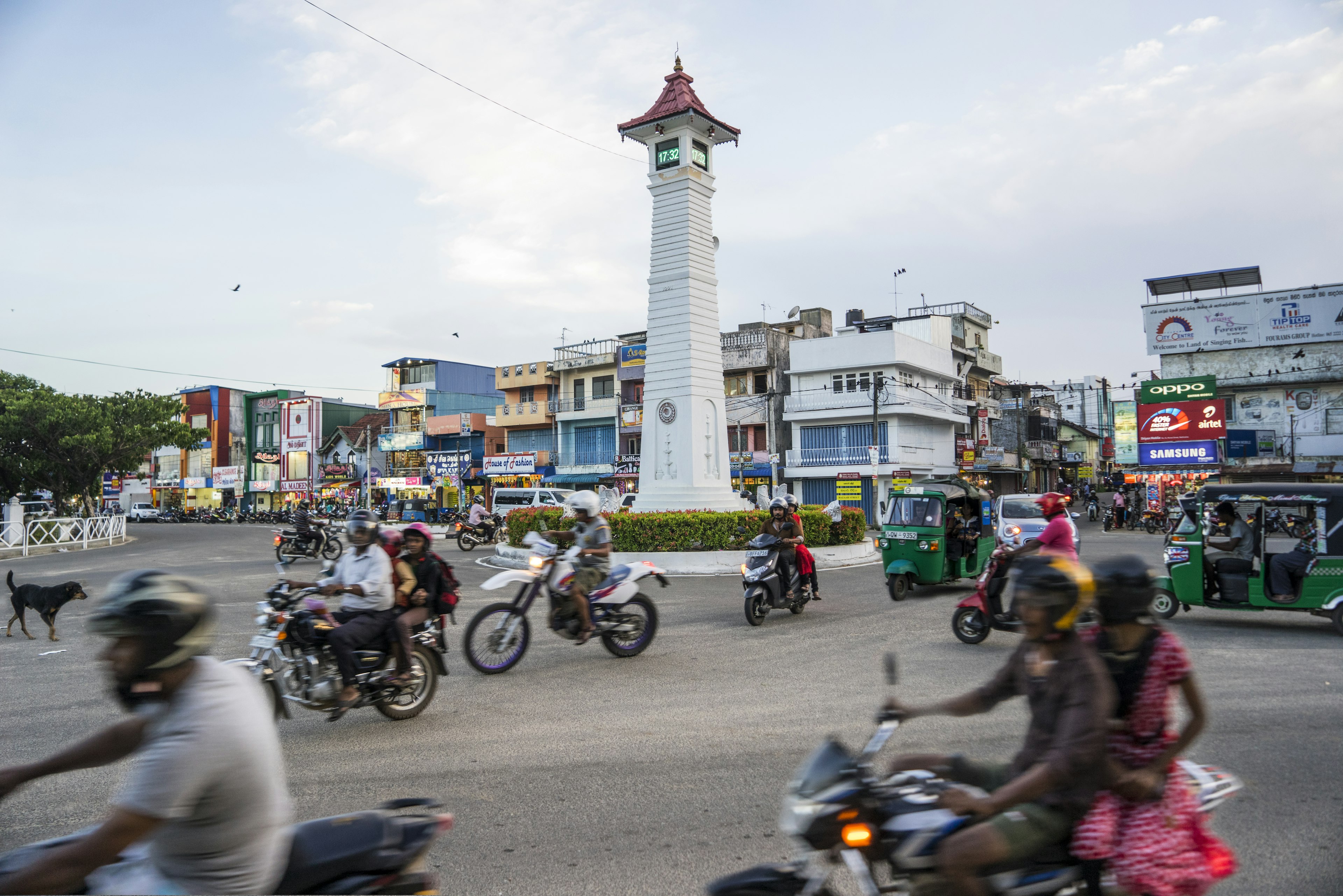 Scooters crowd a roundabout with a tall column on a street in a South Asian city