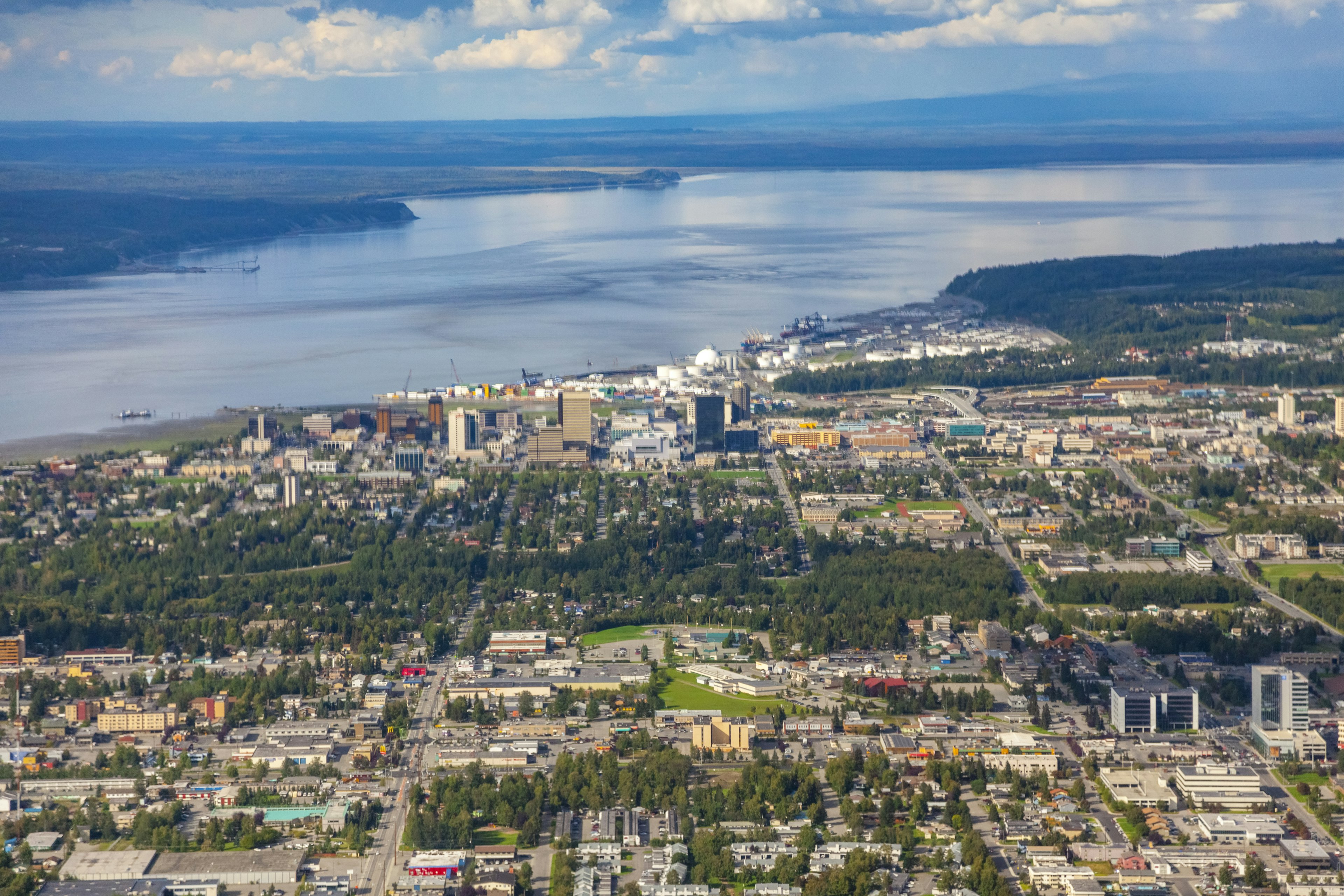 An aerial view of Anchorage, Alaska, showing the towers of downtown, residential areas filled with trees and the water beyond