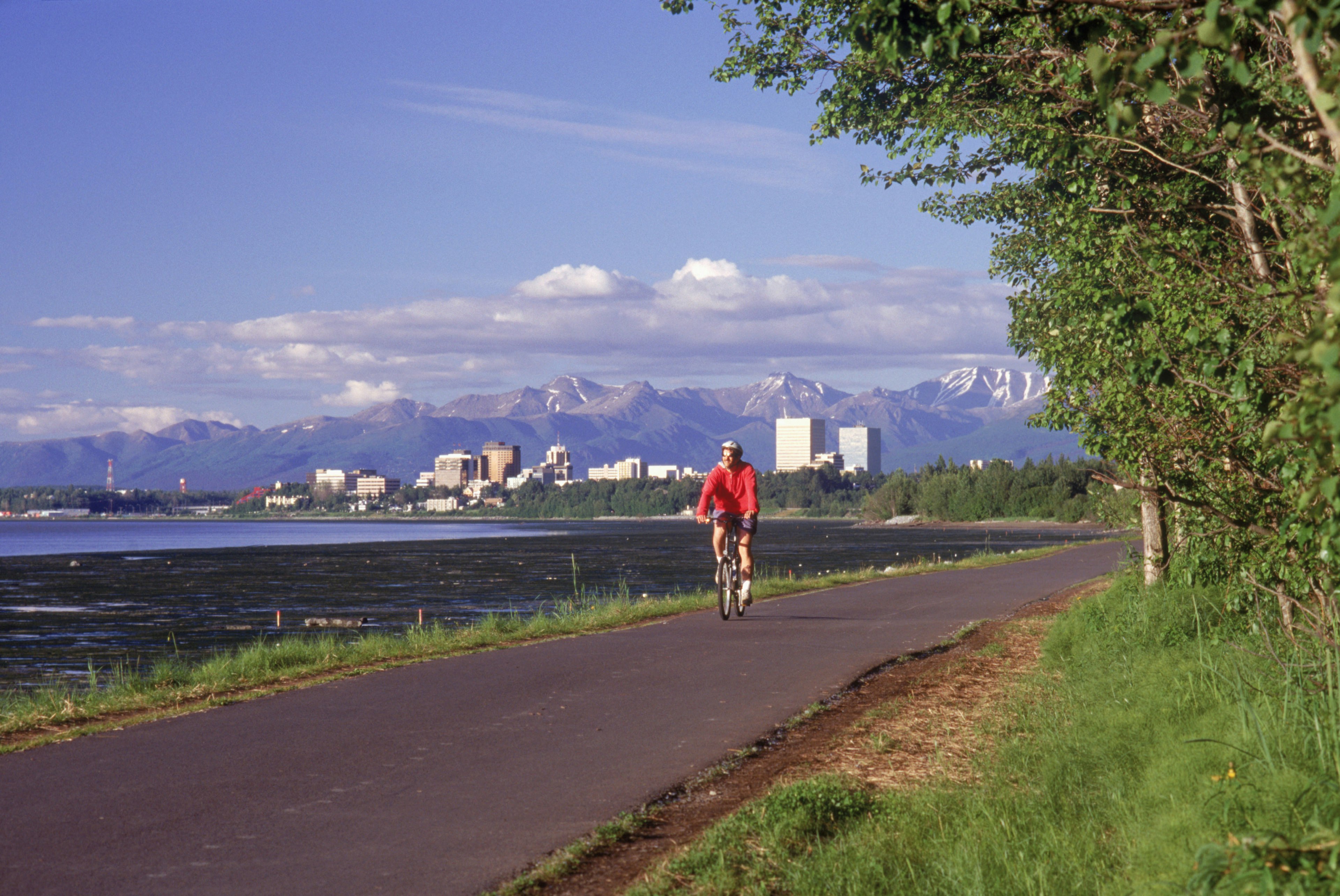 A cyclist on a coastal trail in Anchorage with the city skyline beyond.