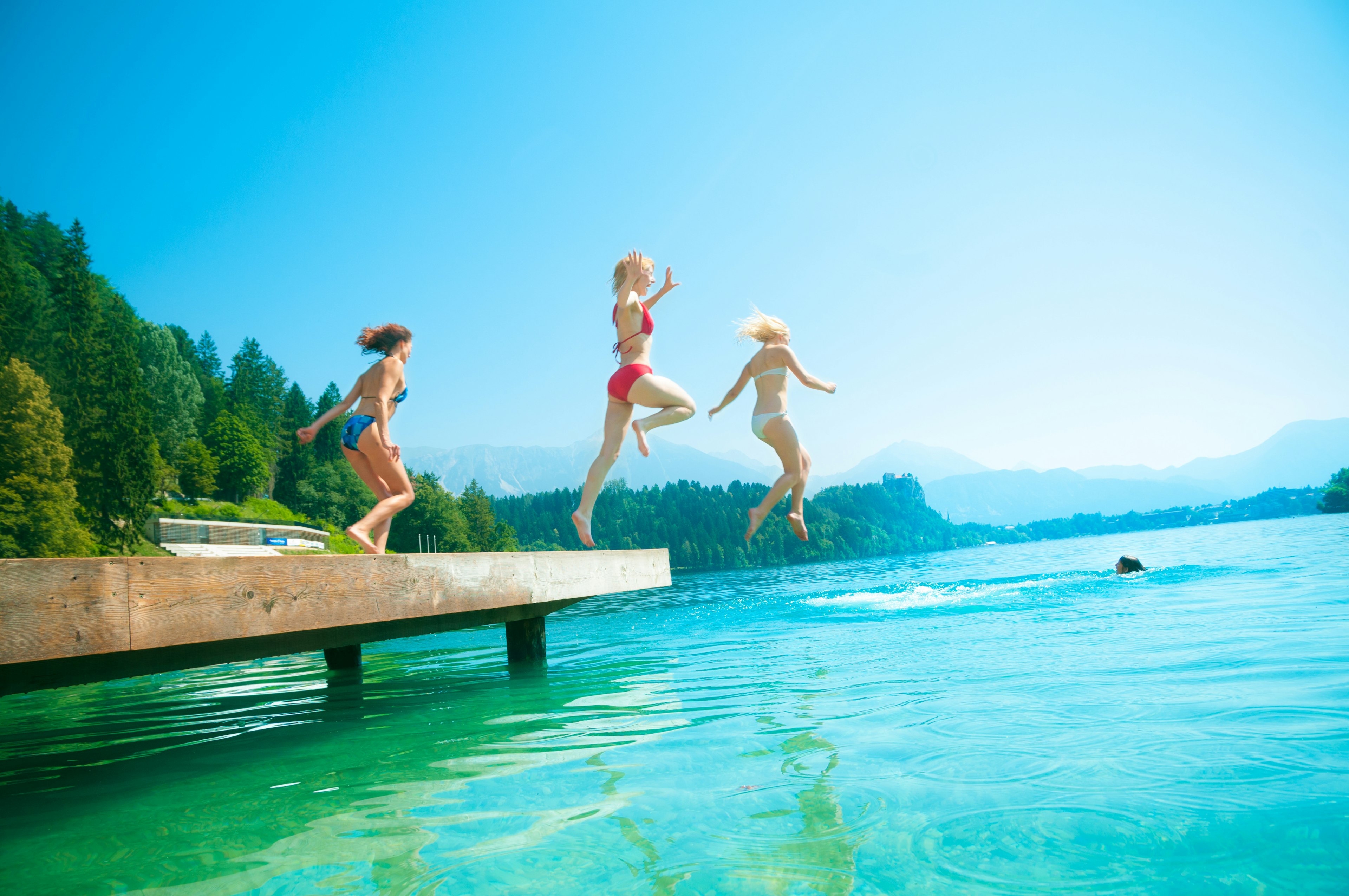 Three girls jumping from a pier into Lake Bled, Slovenia.