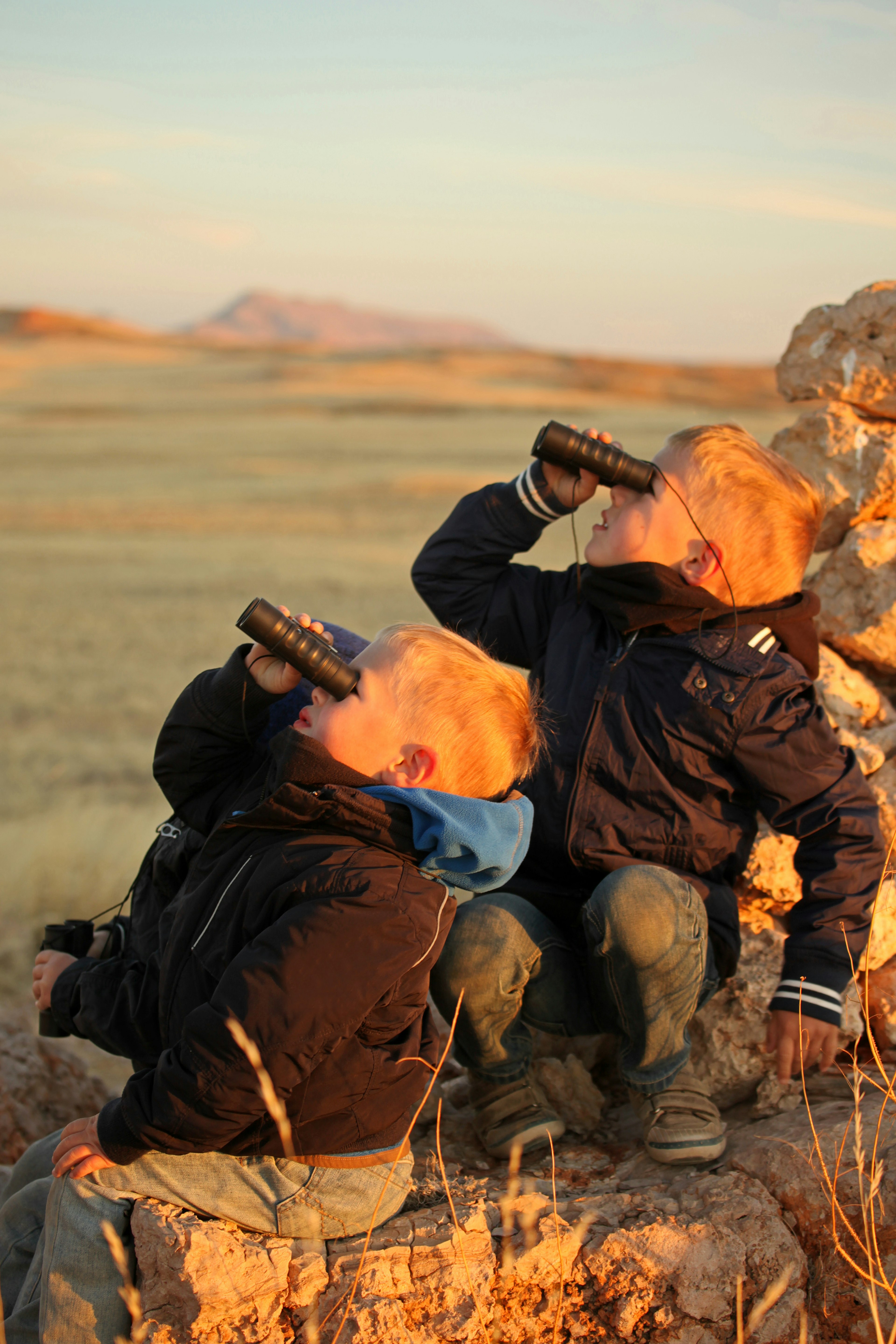 Young boys holding binoculars and watching something high up in the air during a sundowner safari drive in Namibia.