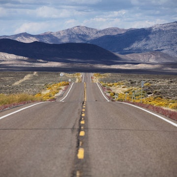 An open road with mountains, hills and vegetation surrounding it.