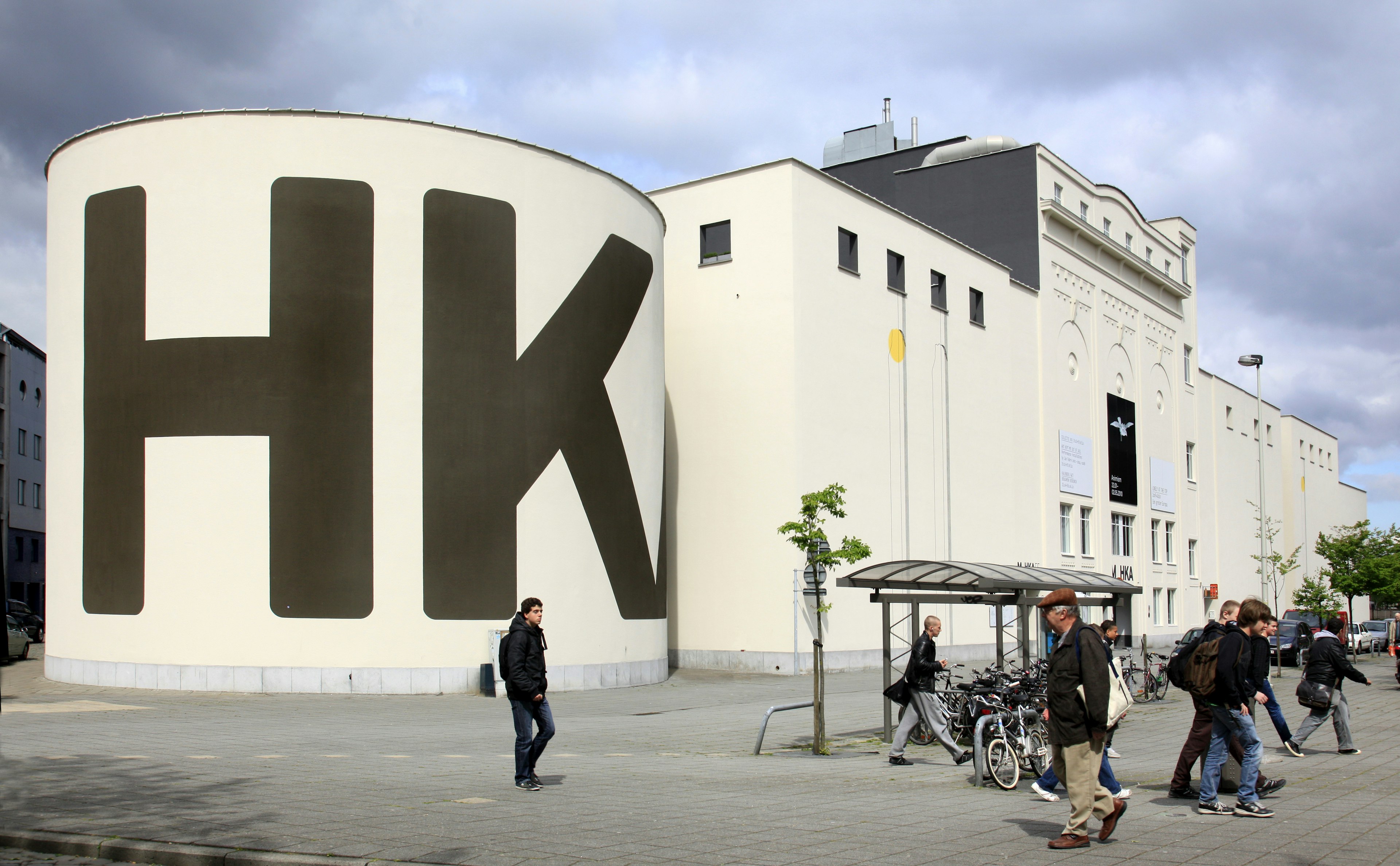 Pedestrians walk by a vast white warehouse building converted into a museum