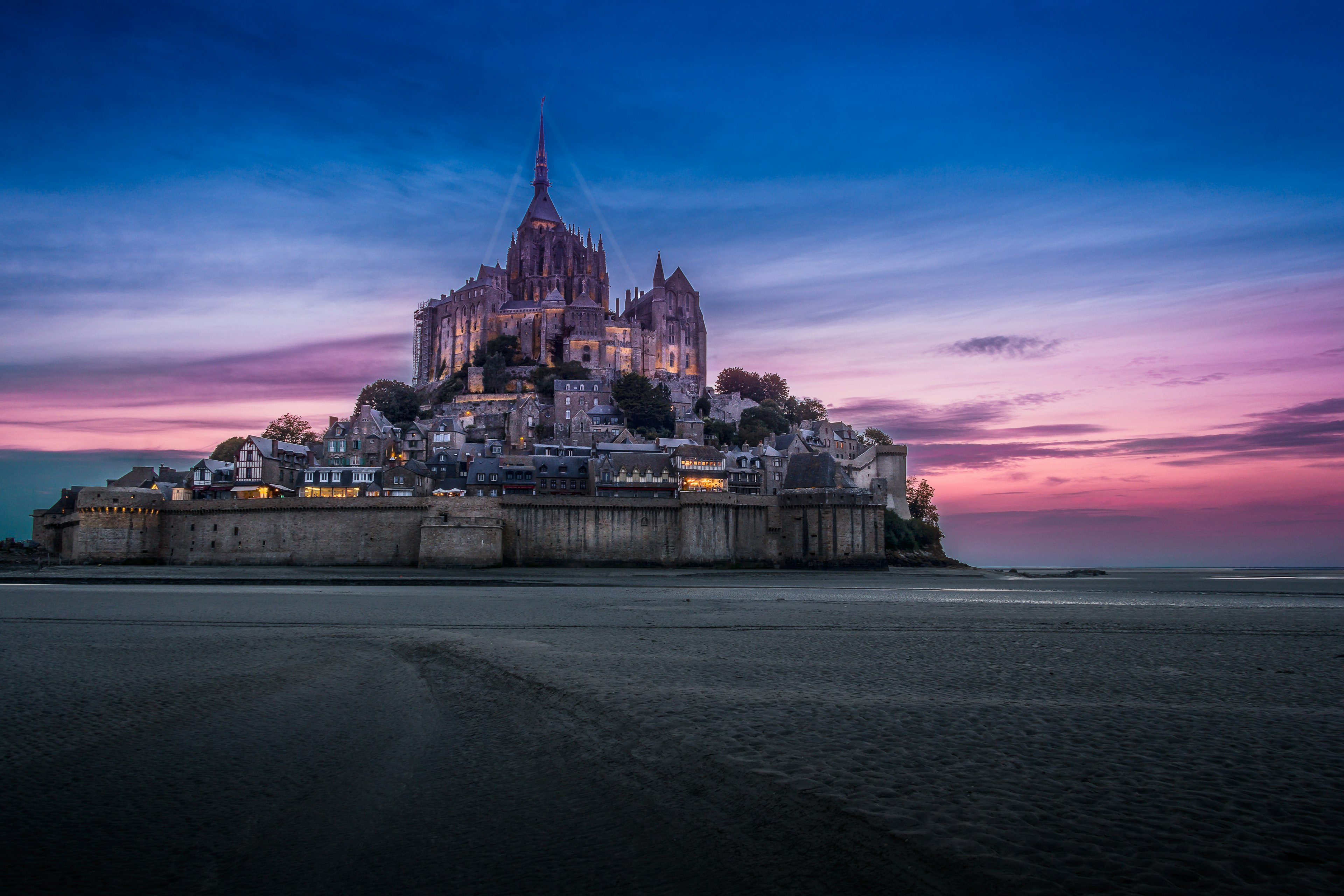 The magical abbey of Mont St-Michel against a very dramatic colourful sunset. The abbey sits across a plain of smooth white sand