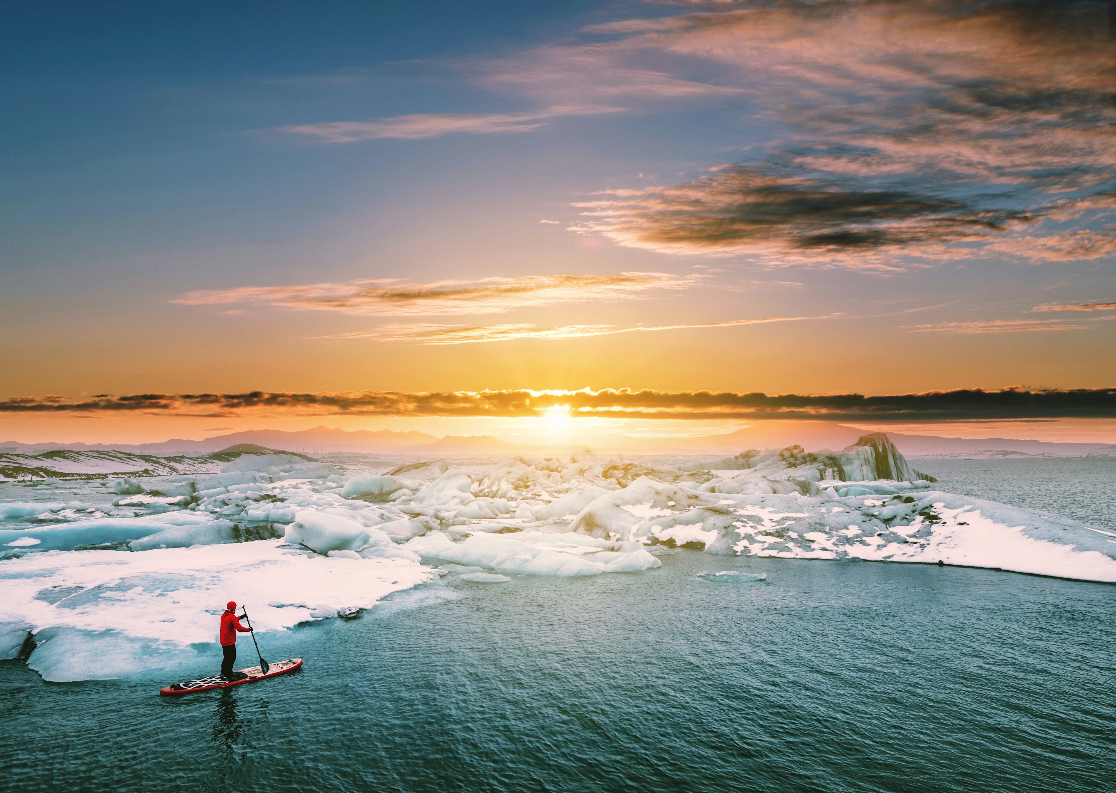 Man paddleboarding in a glacier lagoon during sunset.