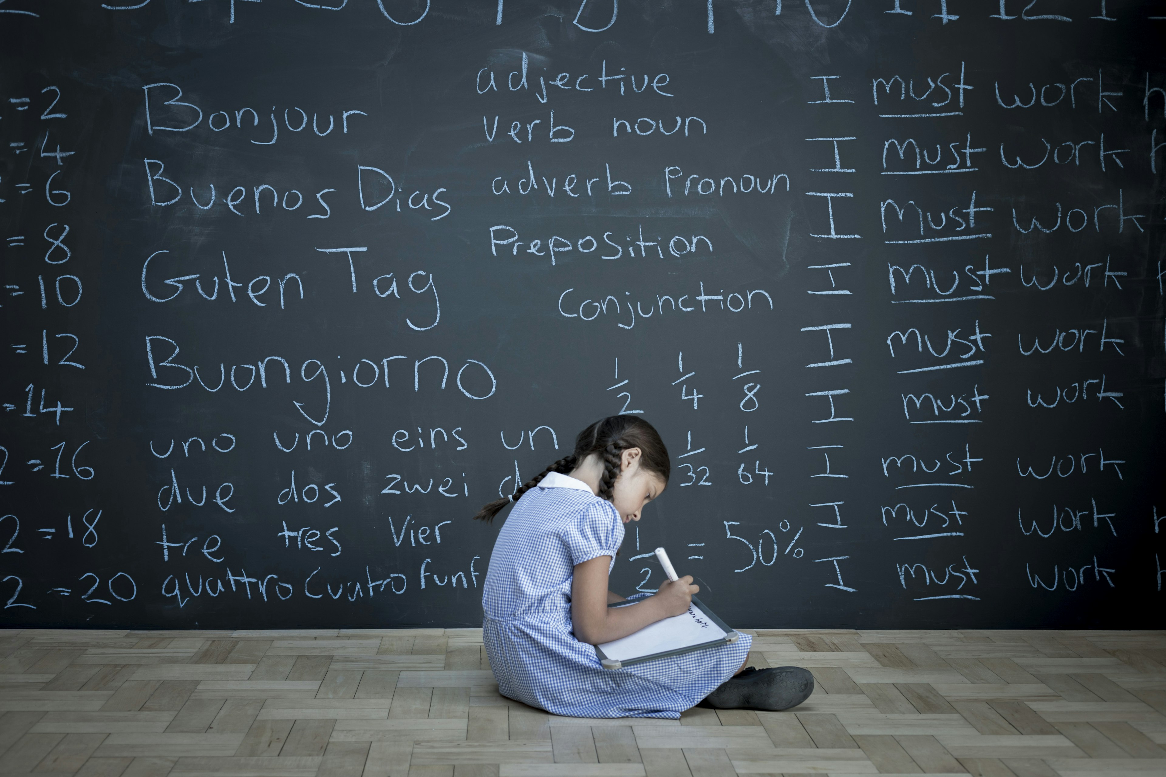 Schoolgirl sitting studying in front of large chalkboard with schoolwork chalked on it