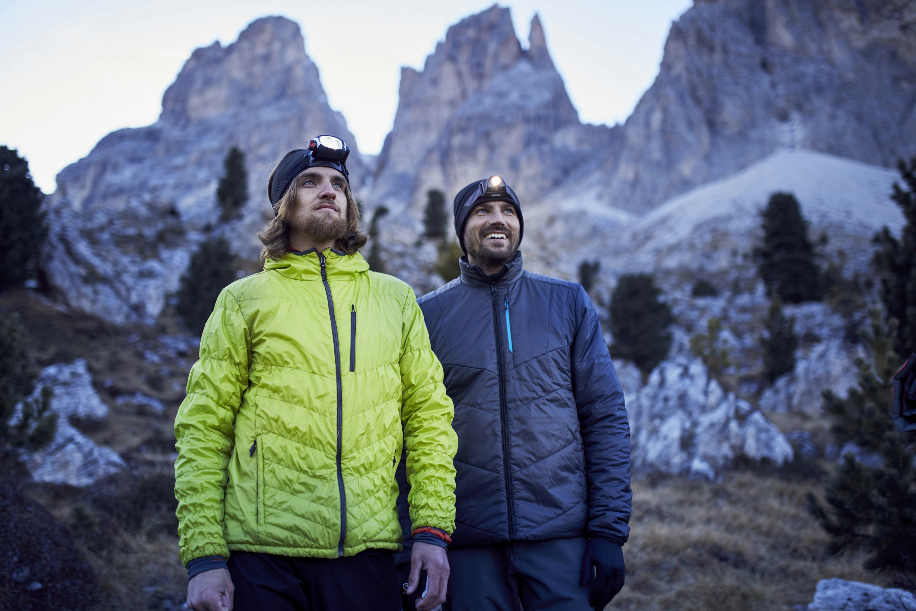 Two men wearing headlamps and jackets standing in a mountains area.