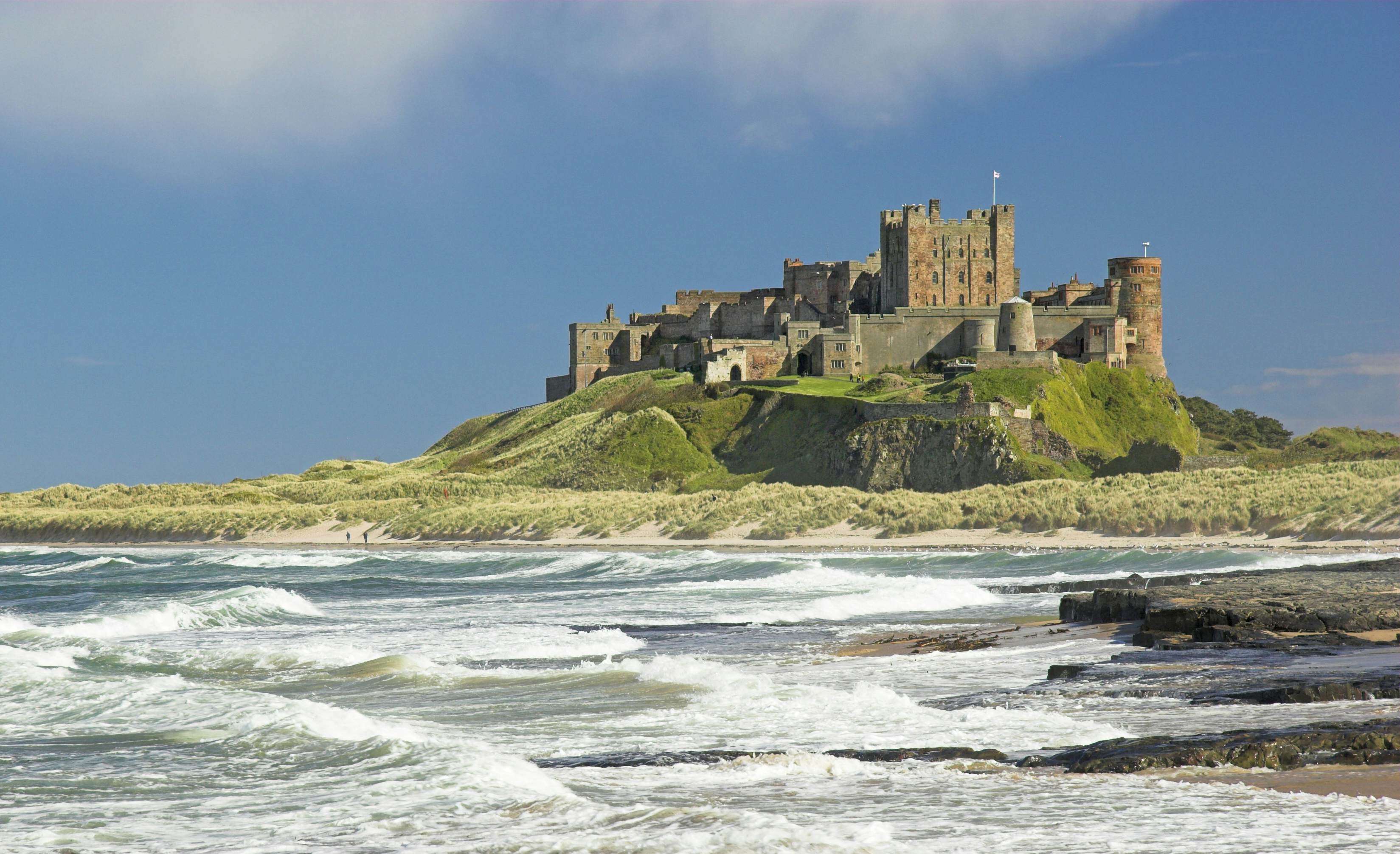 A huge castle sits on a rocky bluff overlooking thrashing waves