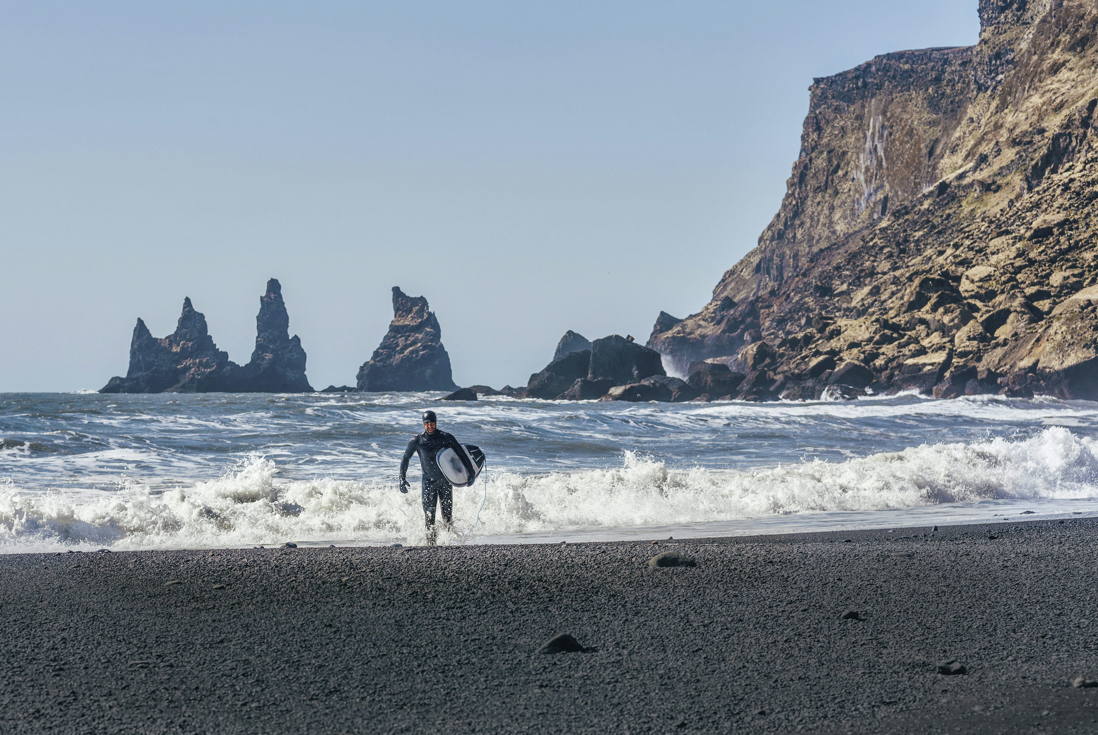 Man with a surfboard leaving the surf at Black Beach on a sunny day.