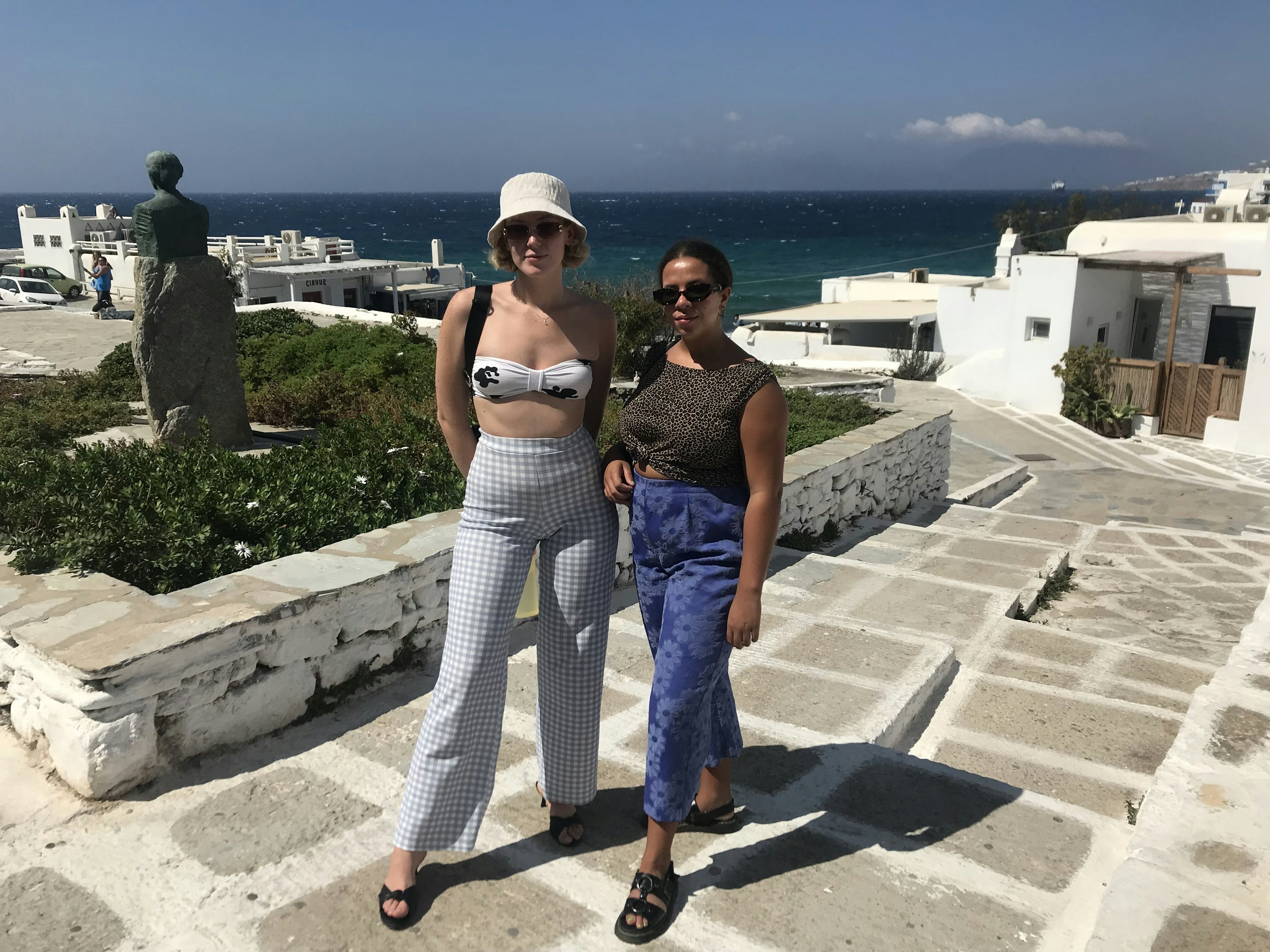 Two women pose for a photo on a stone pathway near the sea