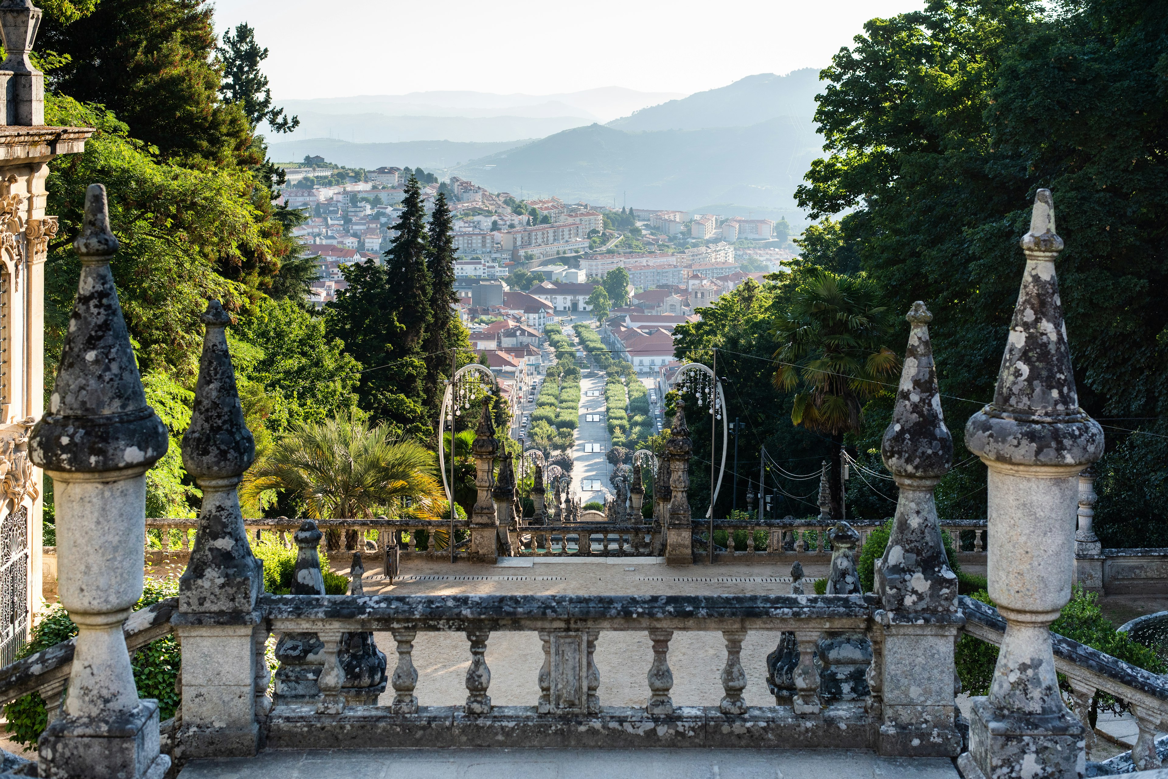 A view from the top of the terrace of Santuário Nossa Senhora dos Remédios, with trees, a village and misty hills in the distance, Lamego, Portugal