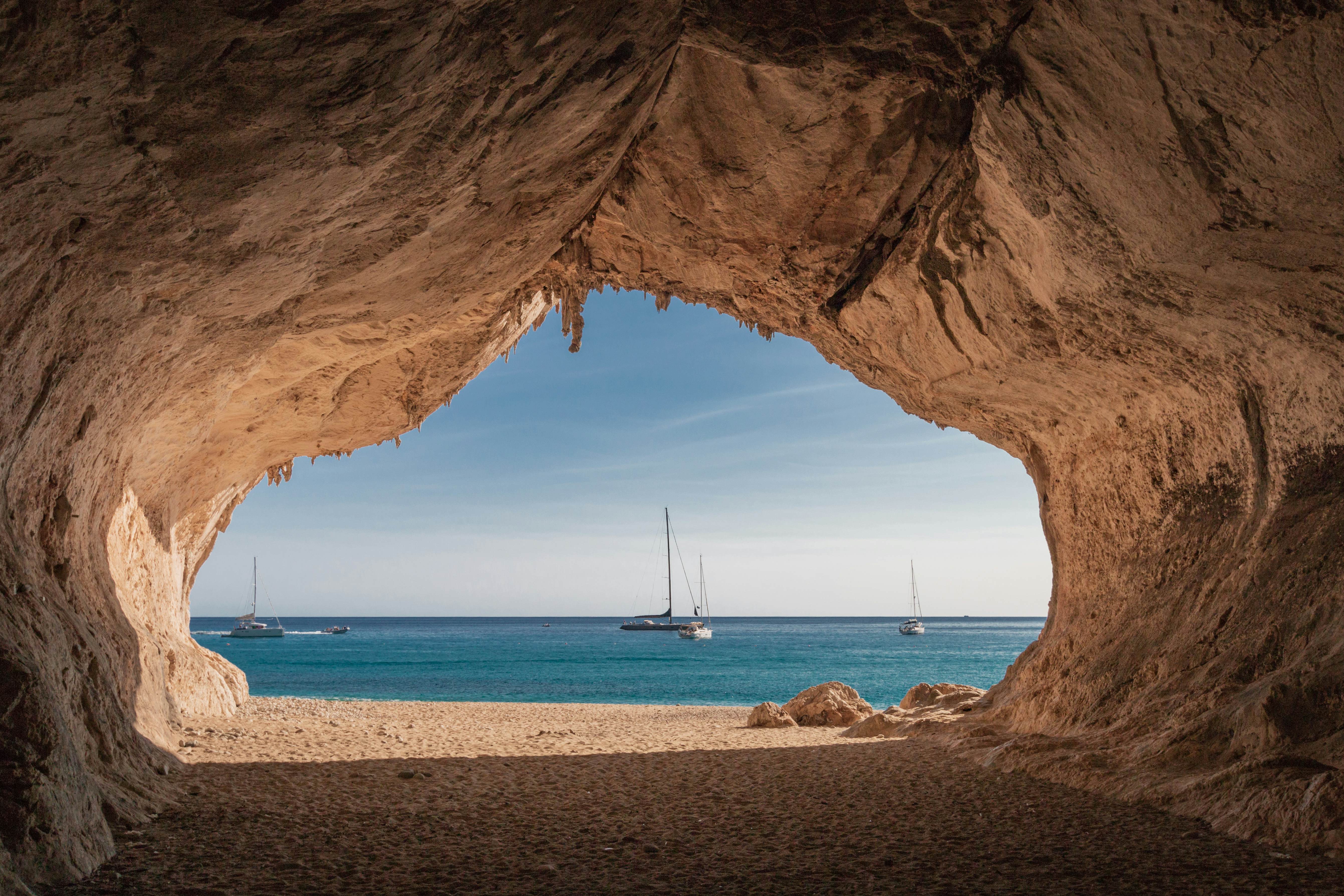 A sandy cave with a view out towards an ocean dotted with sail boats