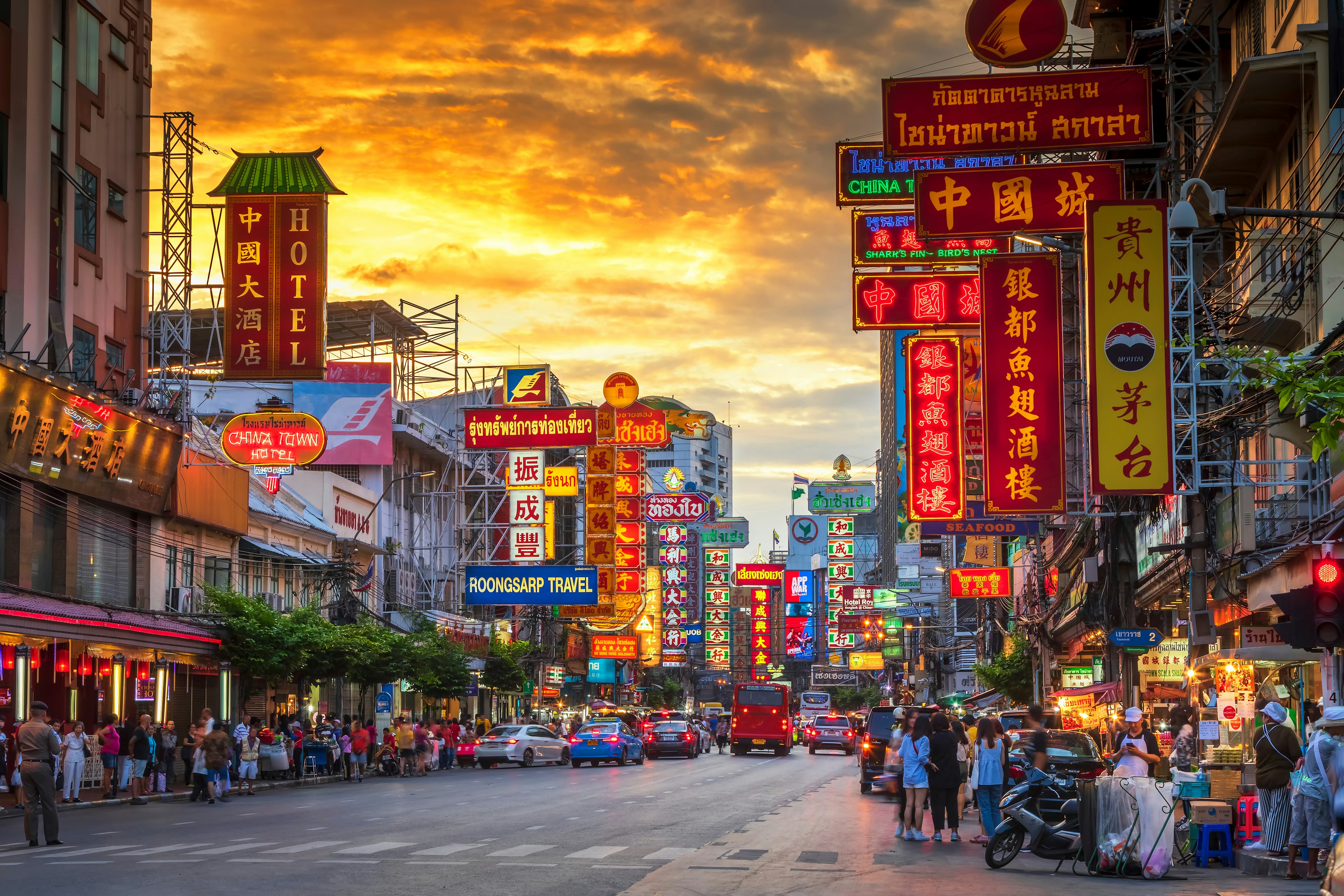 A street lit up with neon signs at night, with people lining up at food stalls