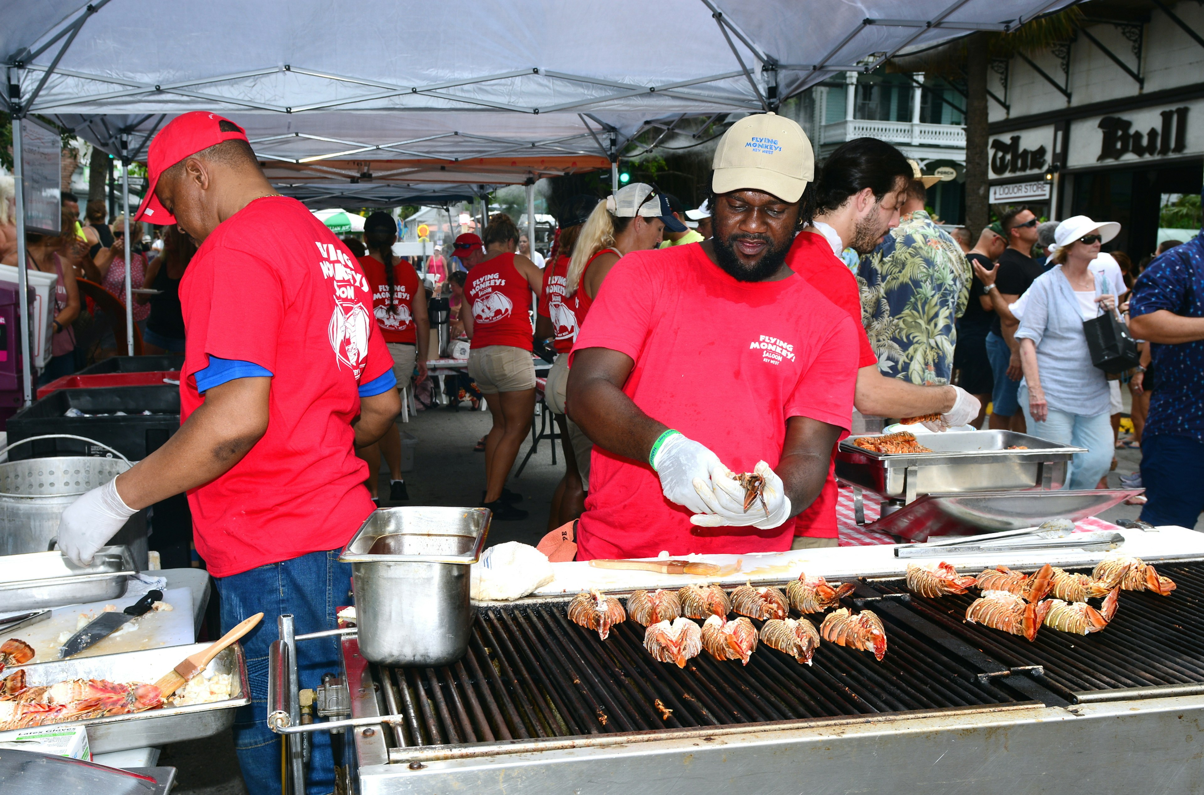 Men tend a grill where Florida spiny lobsters are cooking, as patrons at the Key West Lobster Festival mill in the background