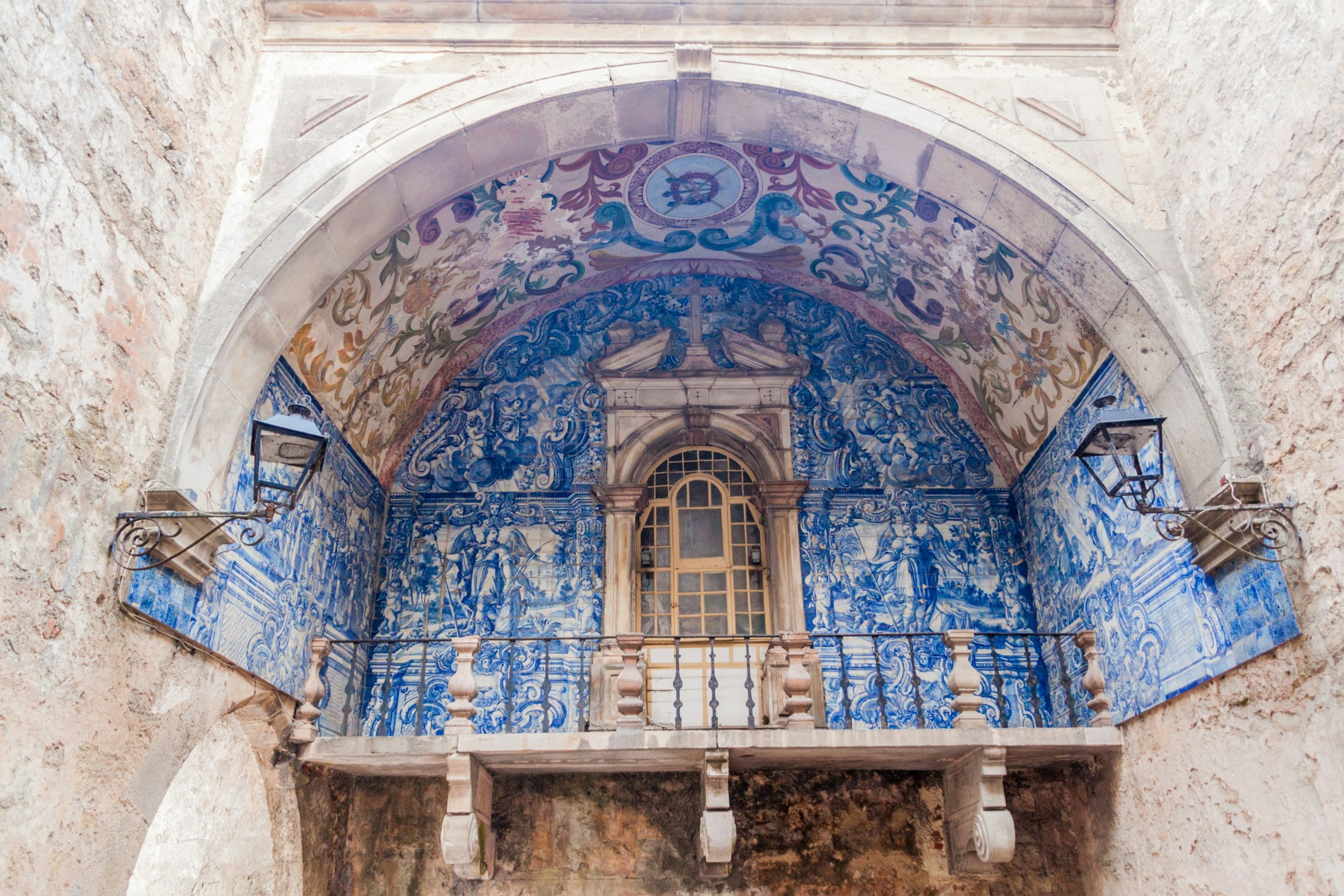 A large arched gateway with a balcony covered in decorative blue and white tiles that depict a visual story