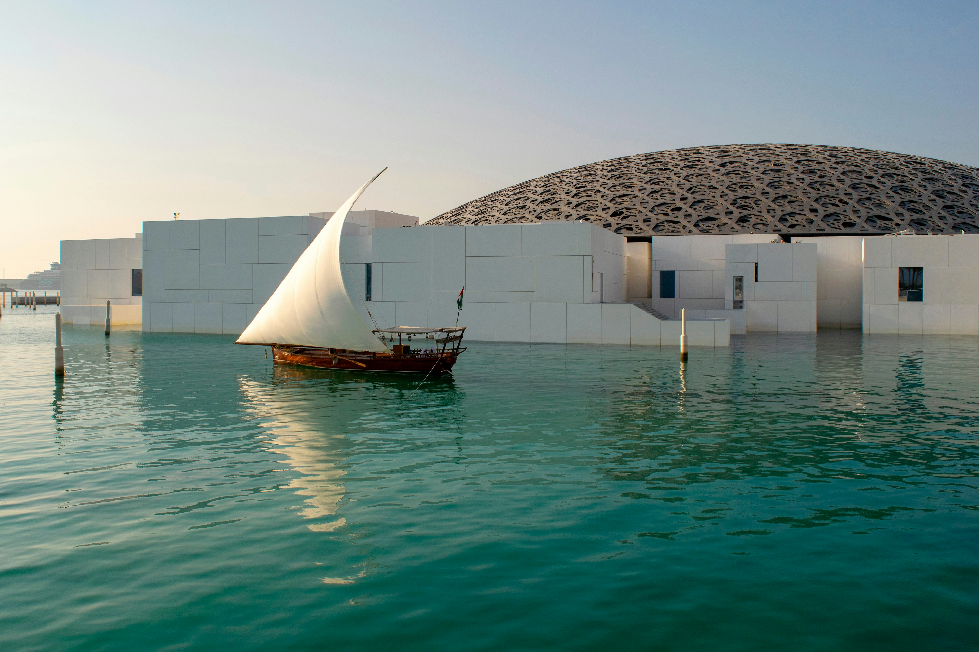 View of beautiful Louvre exterior with waterfront and wooden sailboat.