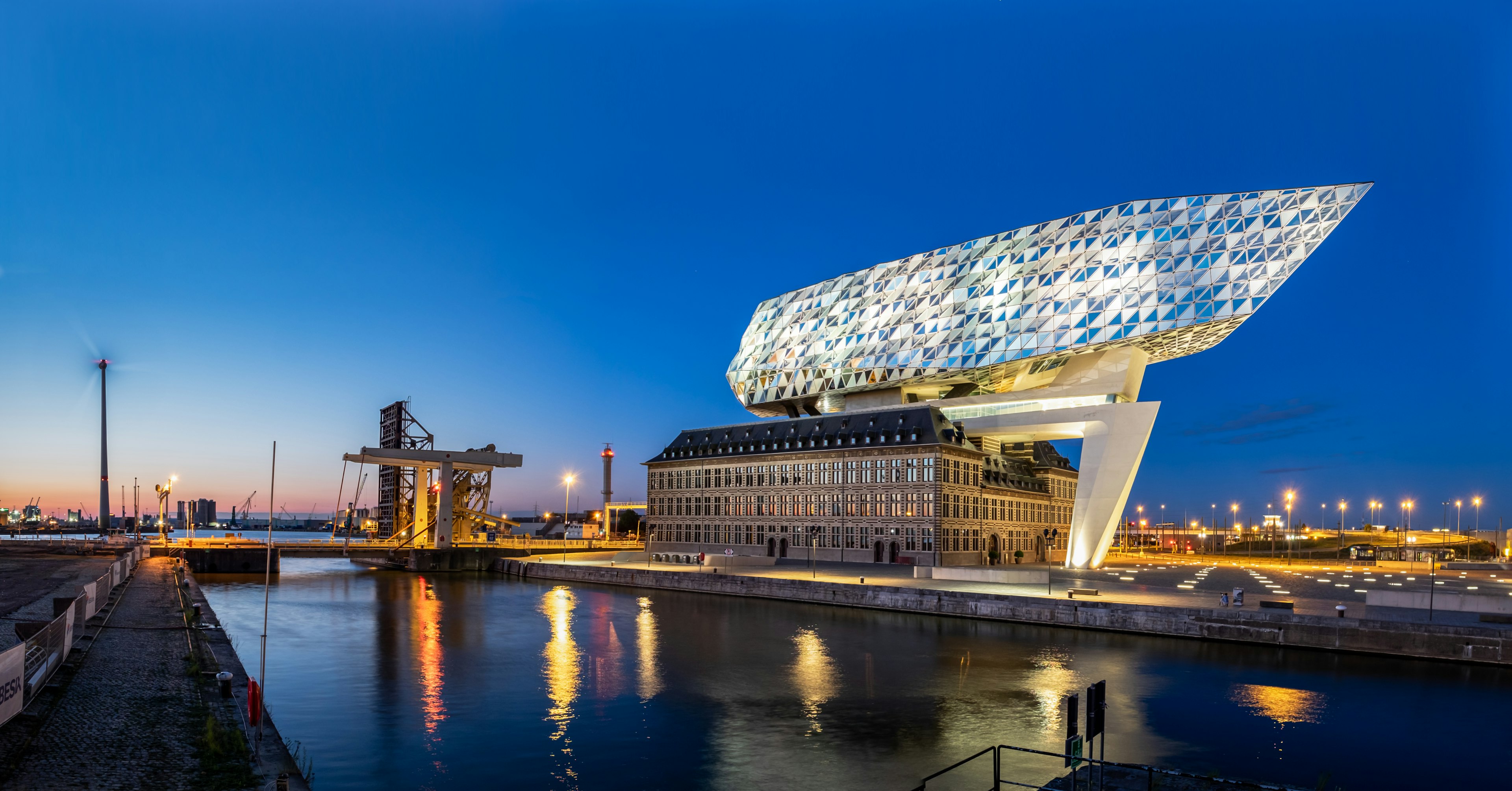 A large glass and steel diamond-shaped structure comes out of the roof of a dockside building