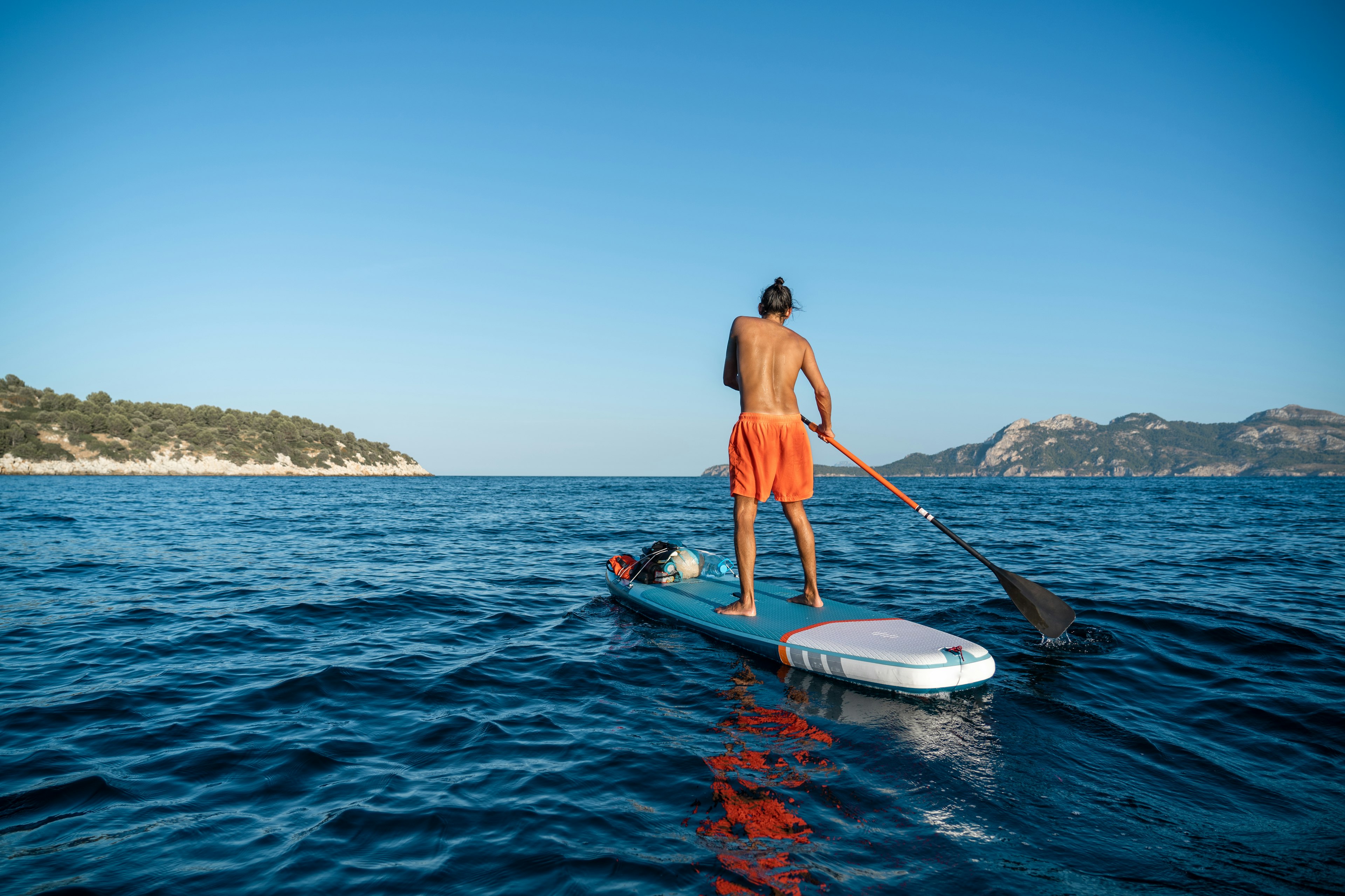 Young spanish man using his SUP on an idyllic place in Formentor, Mallorca (Spain) during a sunny day