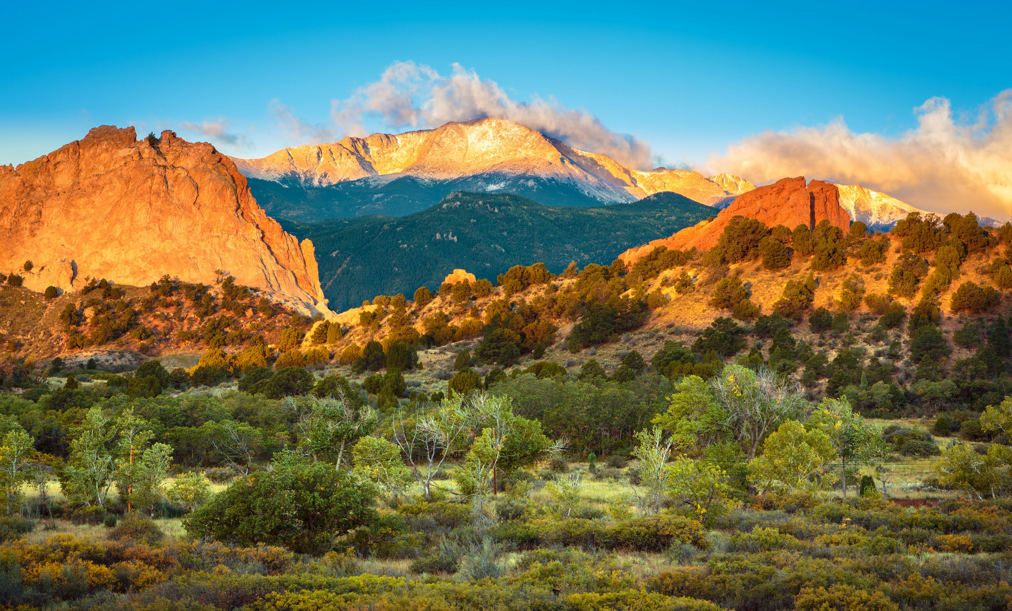 The sun rises towards a series of golden peaks surrounded by changing foliage