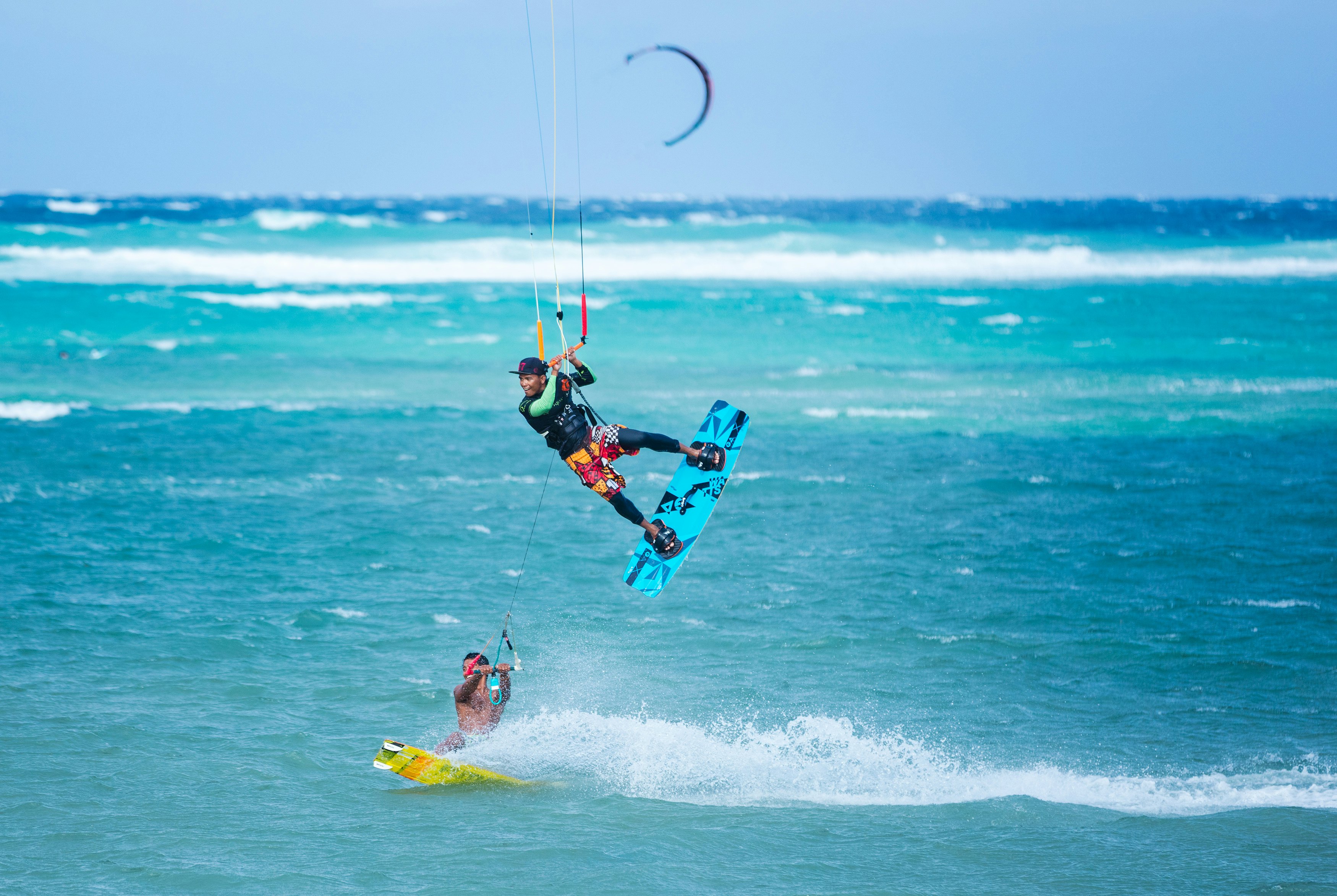 Two kiteboarders using rope tow while riding, one of them performing a jump in blue ocean waters