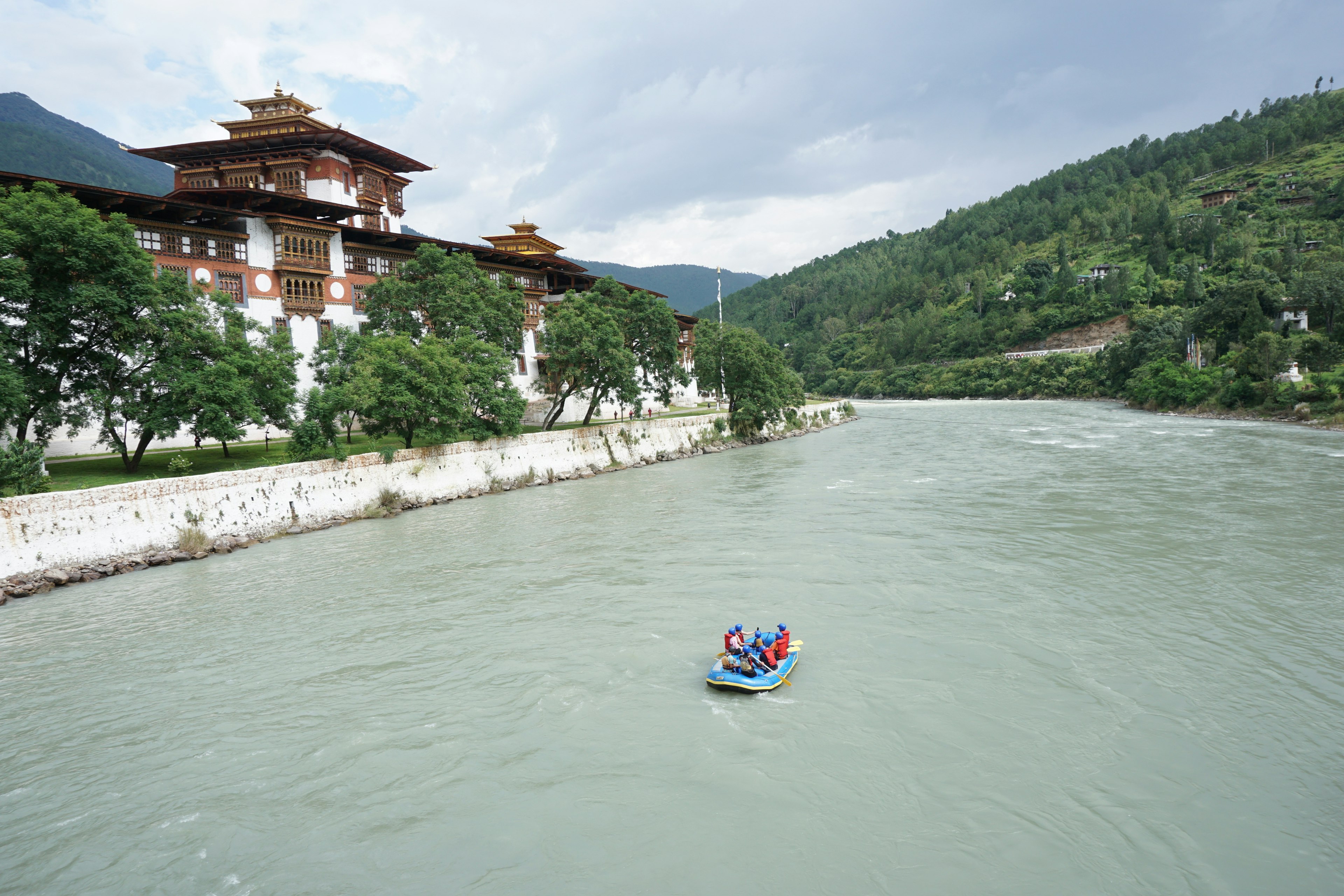 A group of adventurers travels through a river in front of the Punakha Dzong using an Inflatable boat in the evening with cloudy sky.