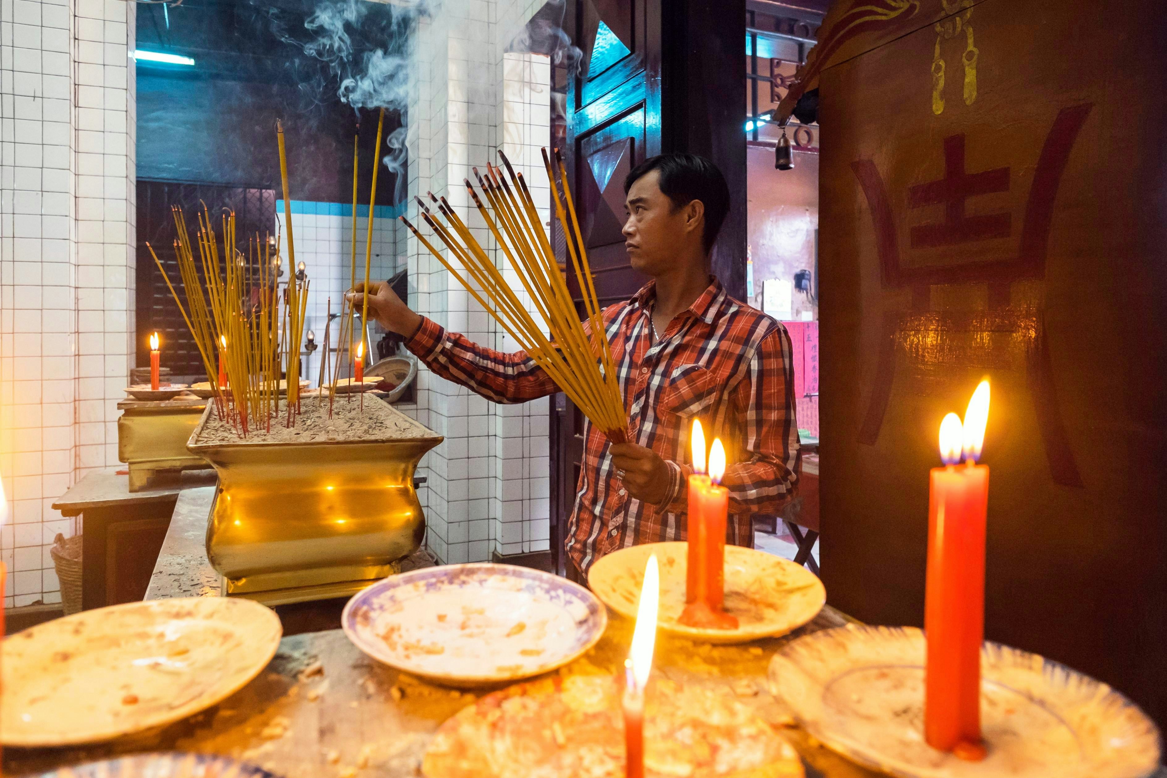 A man lights incense sticks at a Taoist temple, with candles in the foreground, Ho Chi Minh City, Vietnam