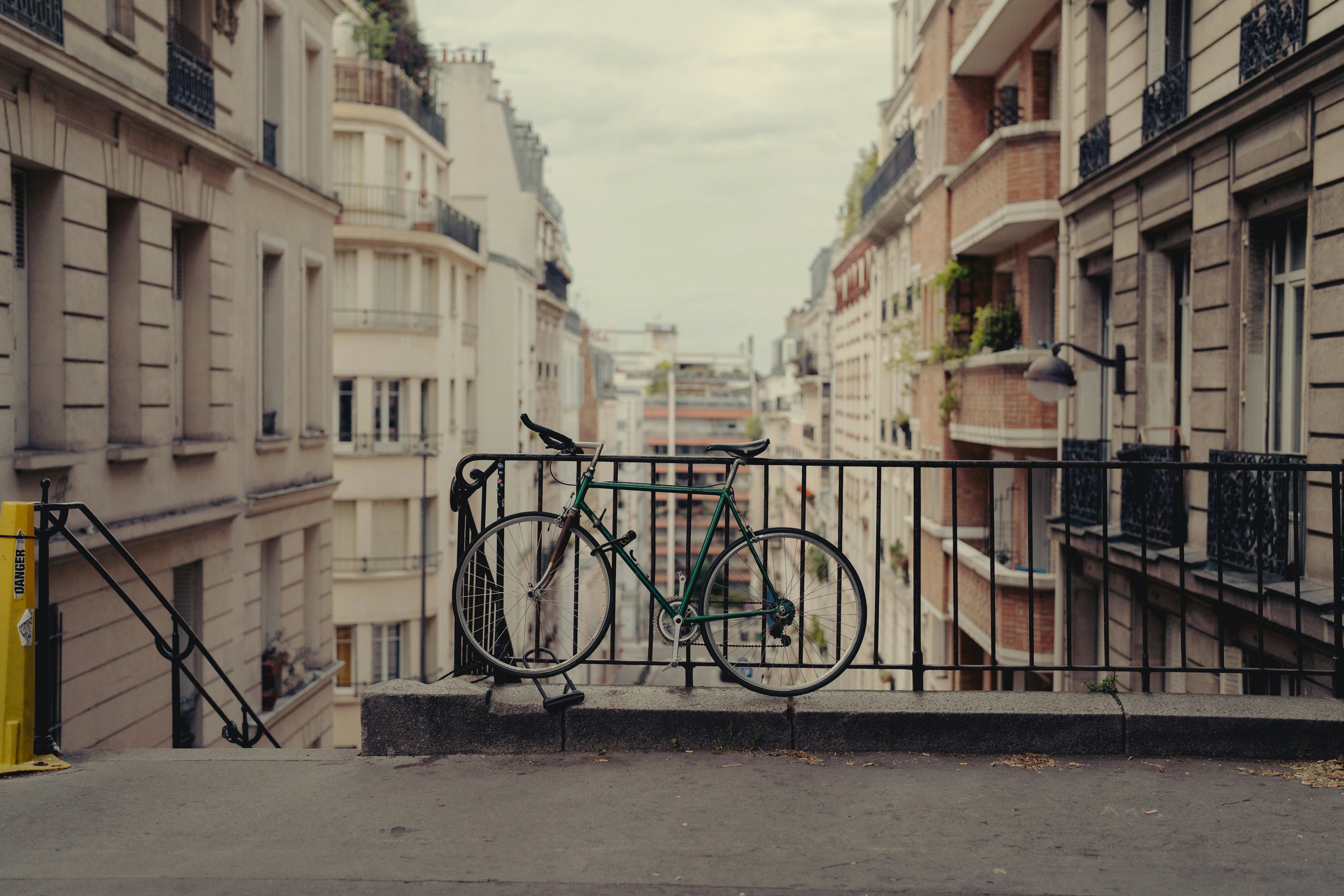 A bicycle is locked to a fence on a public set of steps leading down a hill among buildings in the 18th arrondissement of Paris, France