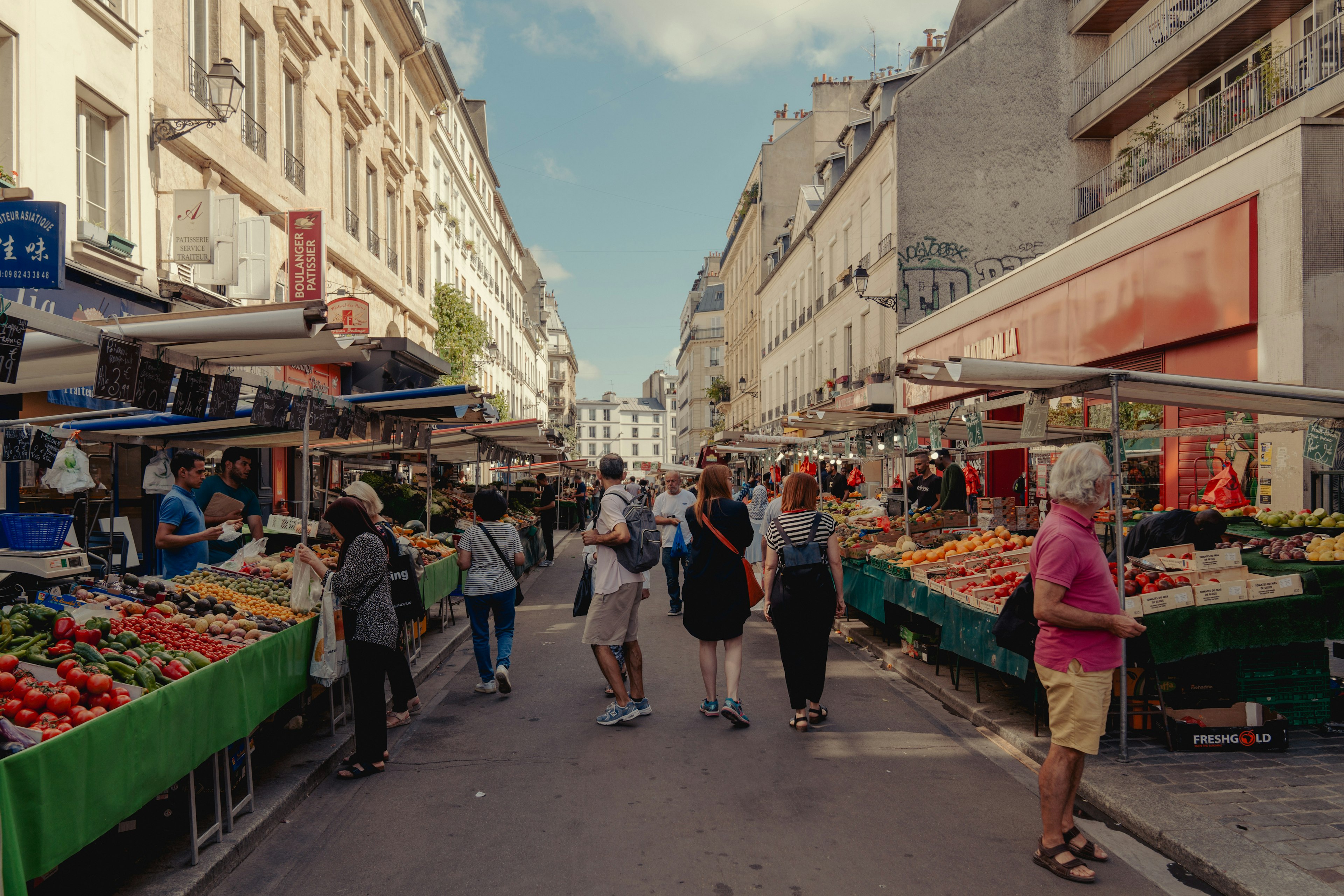 A fresh food market with stalls lining a street and shoppers browsing