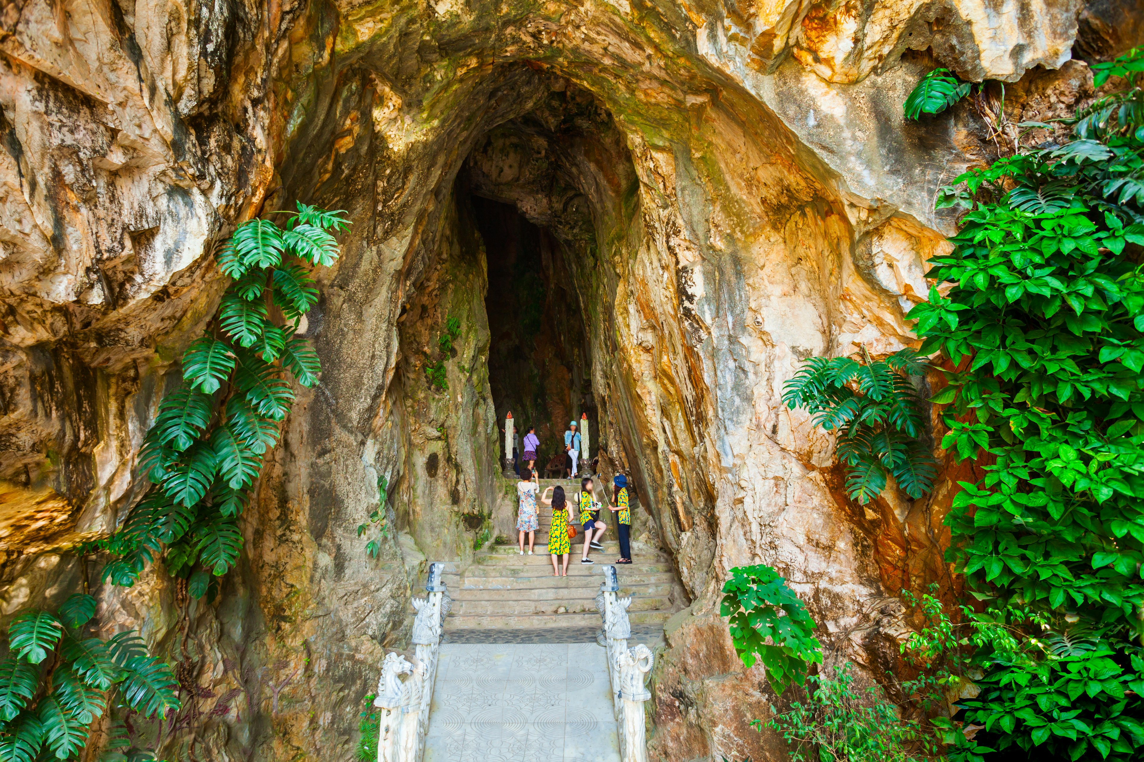 Tourists pause to take photos at the top of a stairway at the entrance to a mountain cave