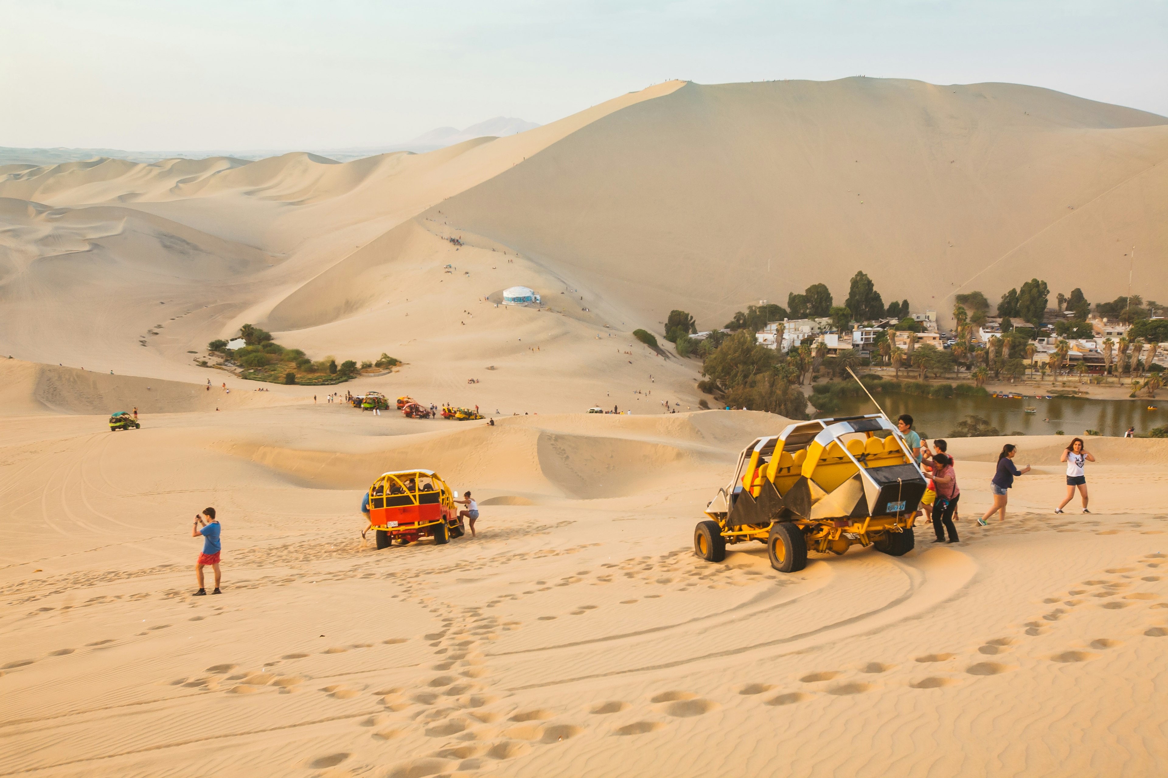 Passengers get out of dune buggies on huge sand dunes above an oasis