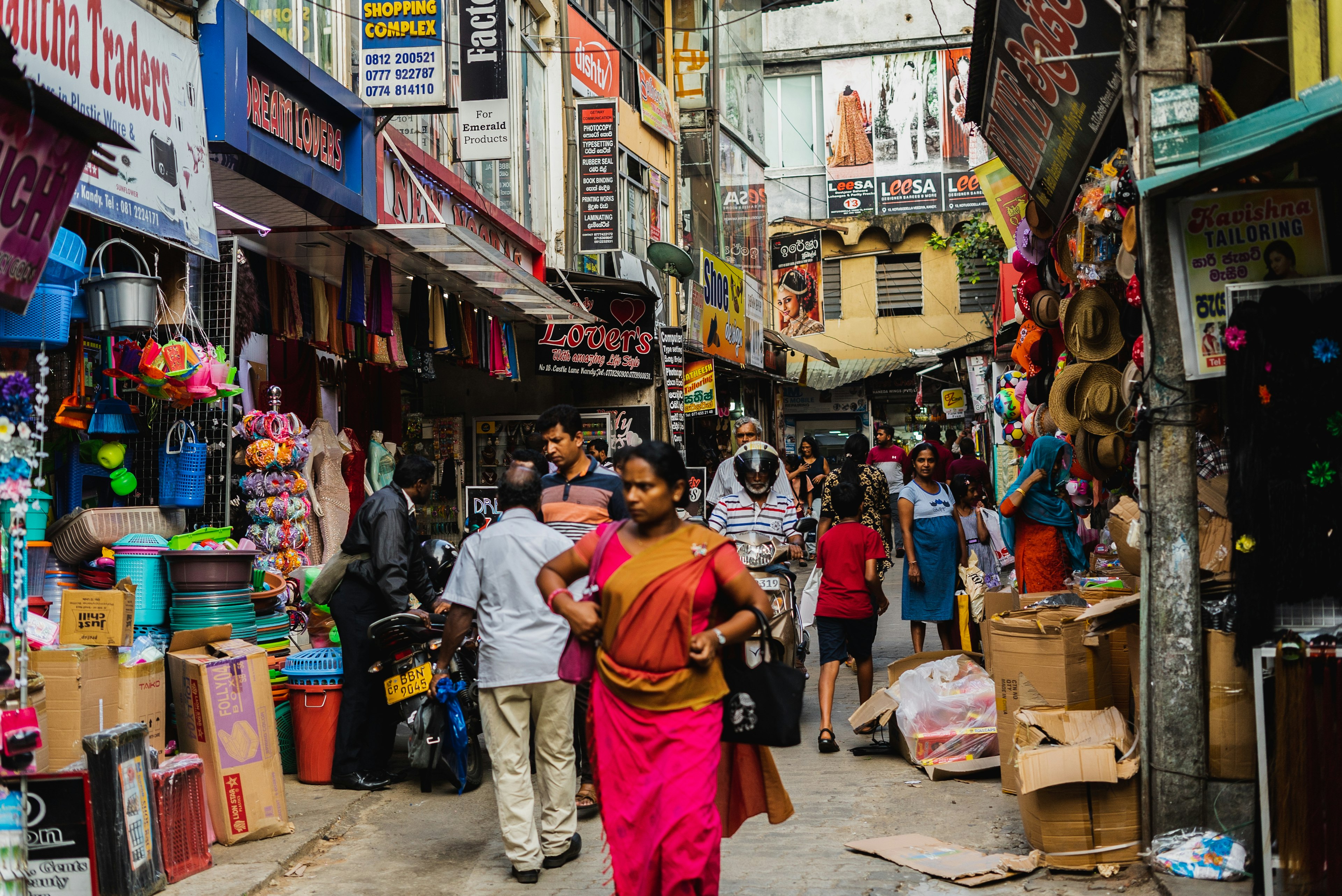 A woman in a pink sari shops on a busy street filled with shops whose merchandise is on display on the pavement