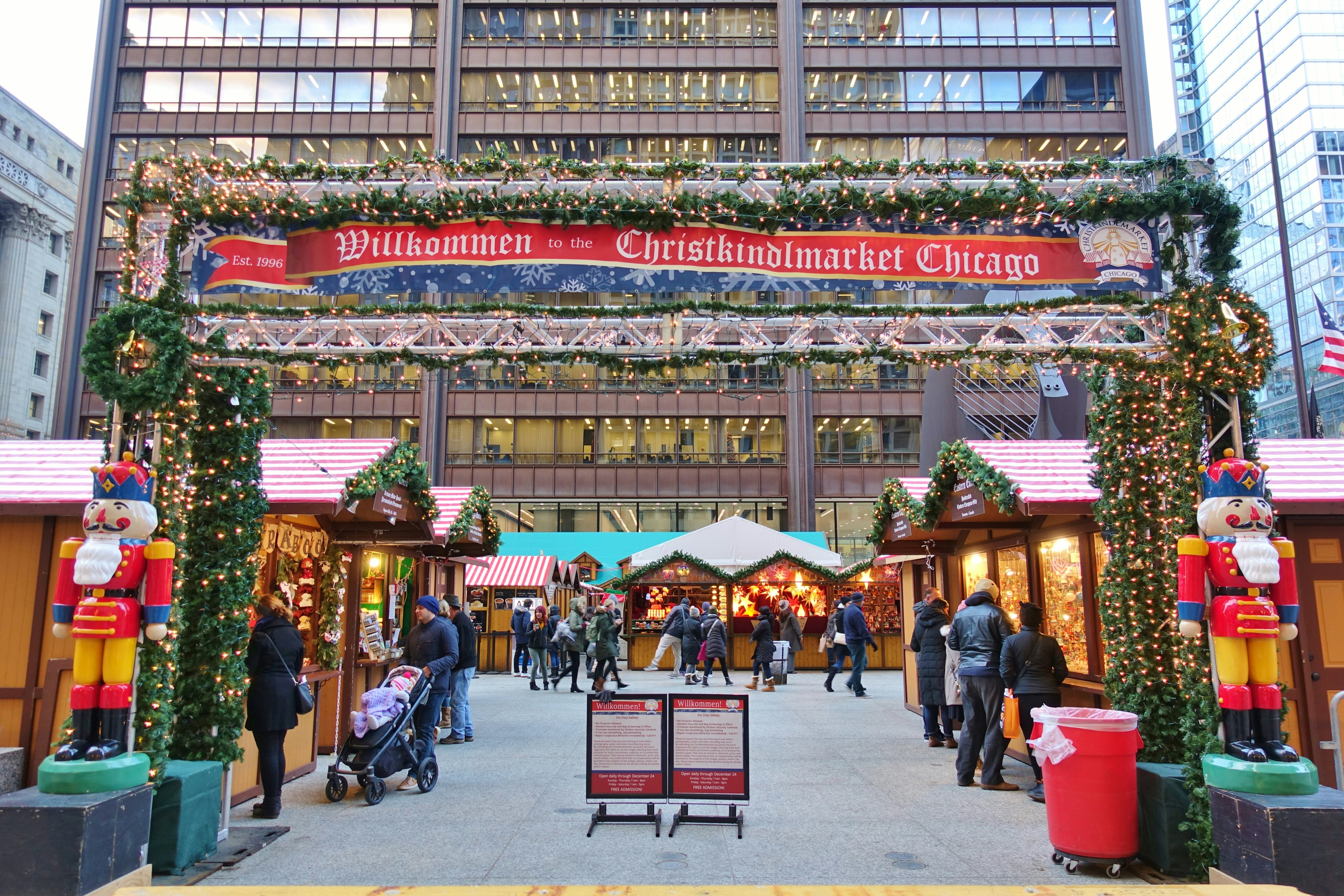 A sign over a series of wooden stalls that reads "Willkommen to the Christkindlmarket Chicago"