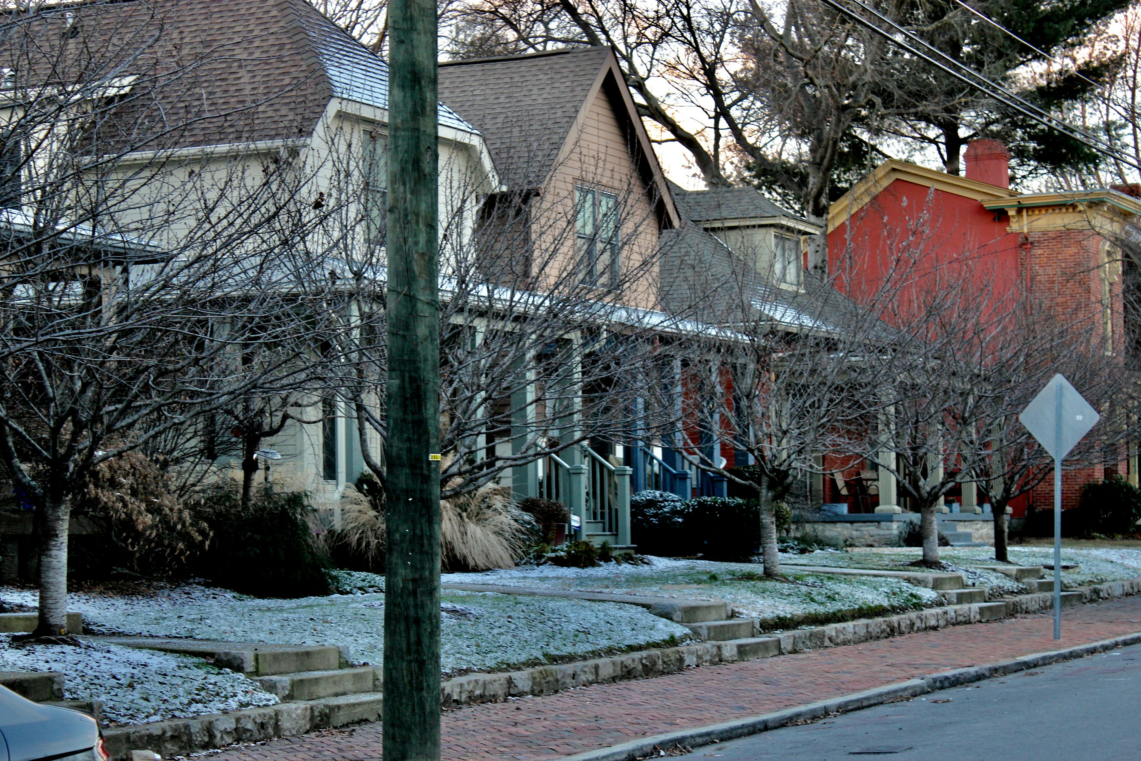 A row of pretty wooden houses with porches on a city street, with a light blanket of snow on their front lawns