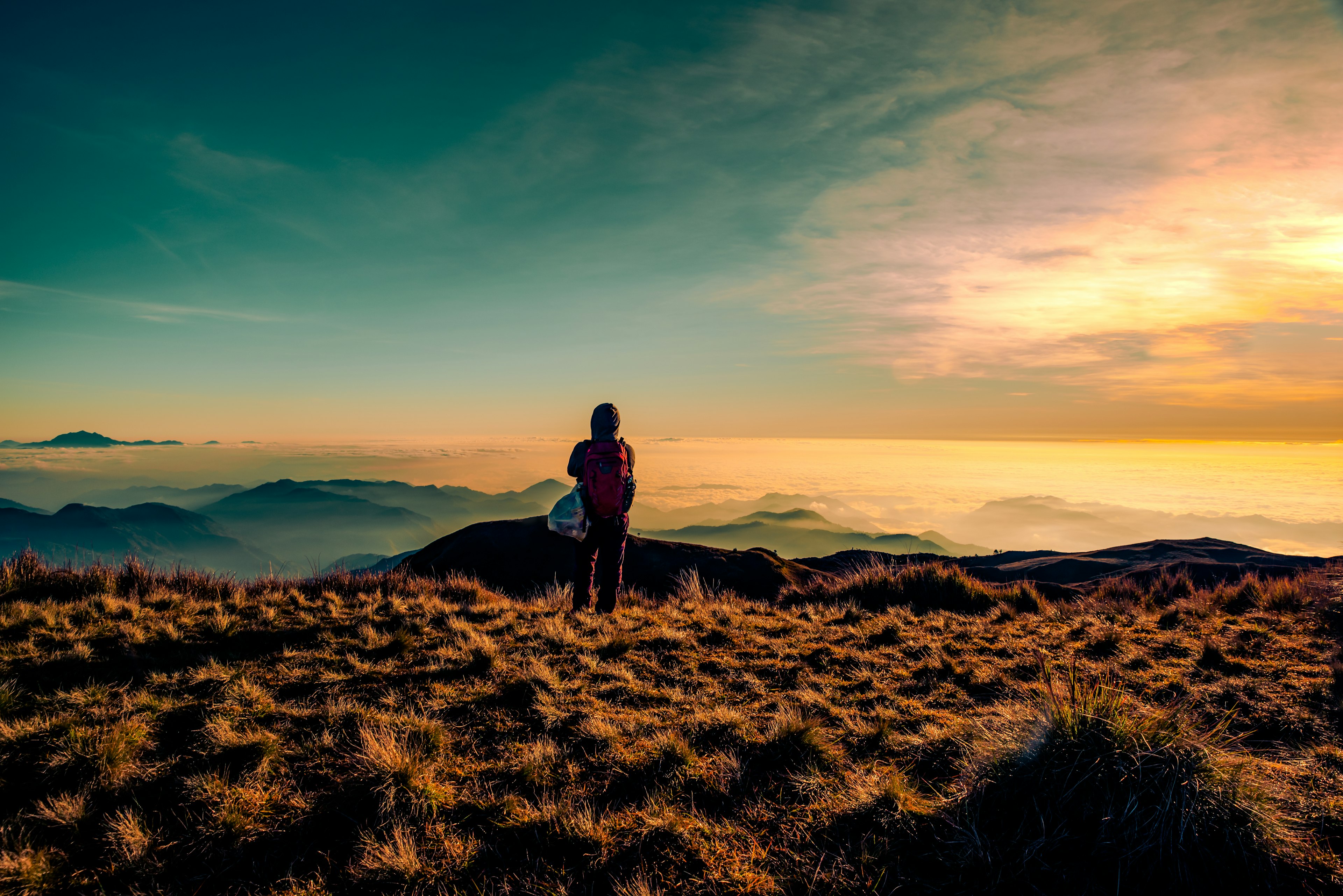 An adult mountaineer standing at the peak of Mt Pulag enjoying the breathtaking view of sea of clouds during sunrise.