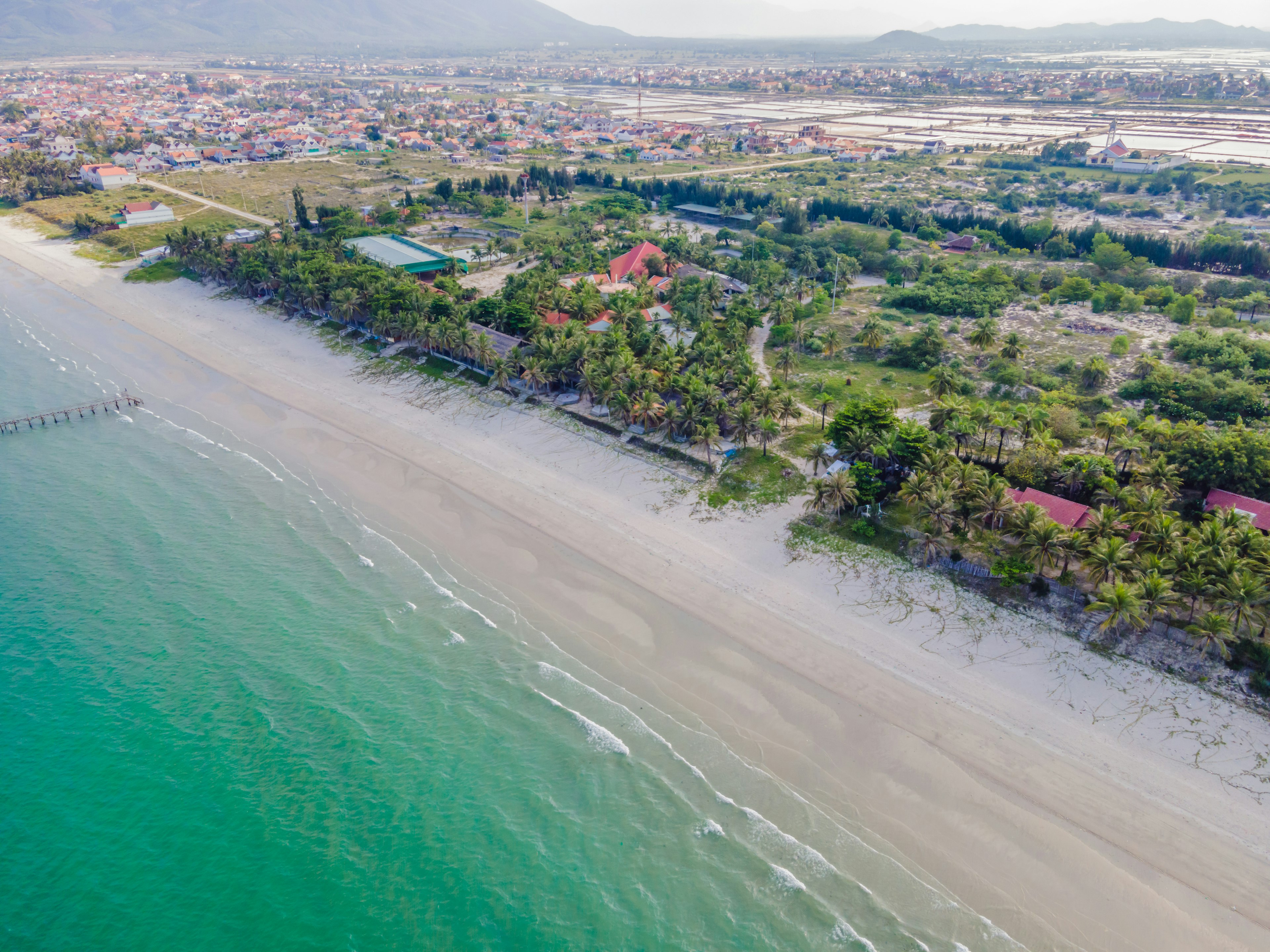 An aerial view of Doc Let beach, with its gentle waves, white sand and palm trees and small houses just in from the shore