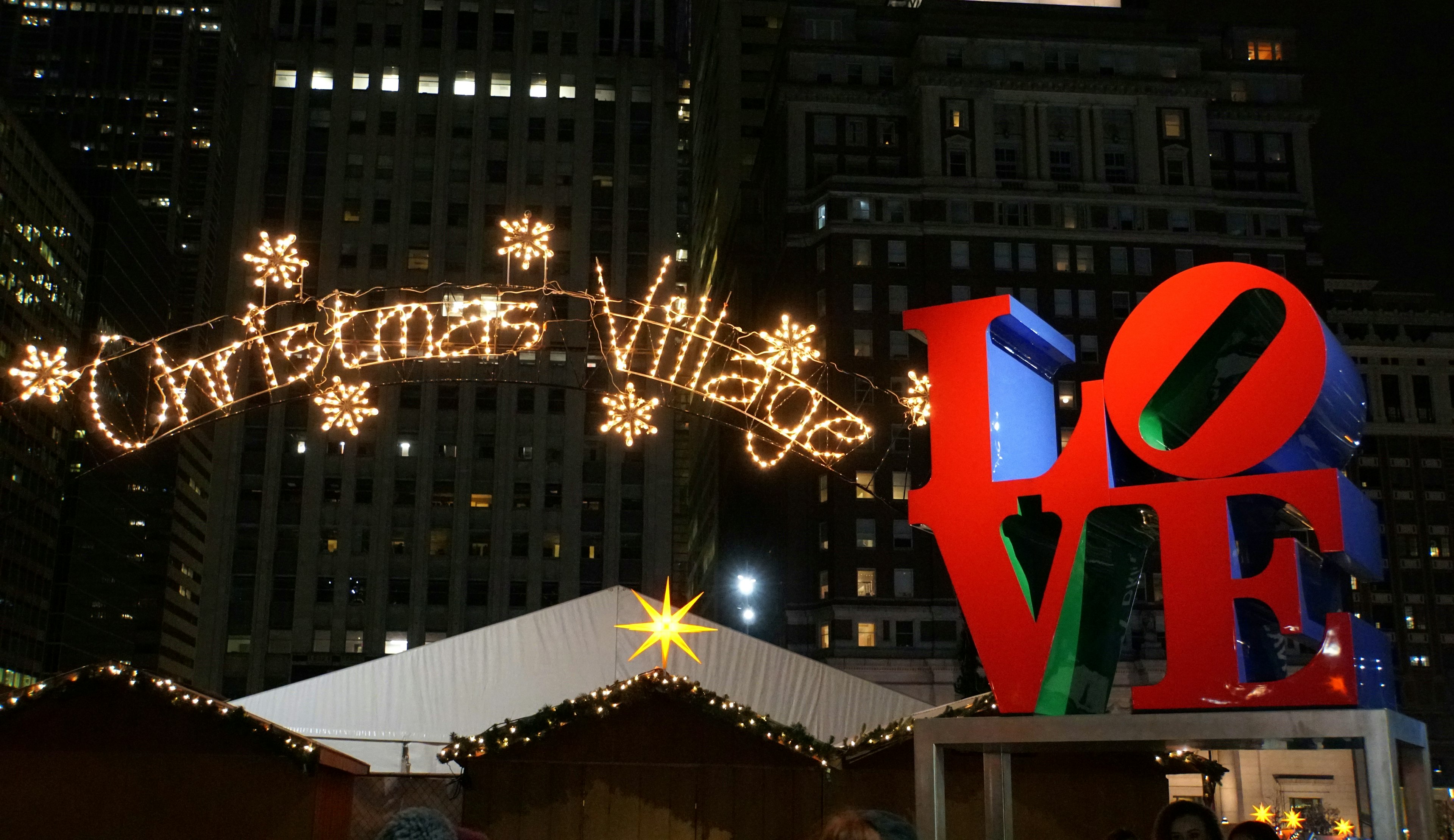 A large lit-up sign that reads "Christmas Village" next to a red sculpture spelling out the word "LOVE"