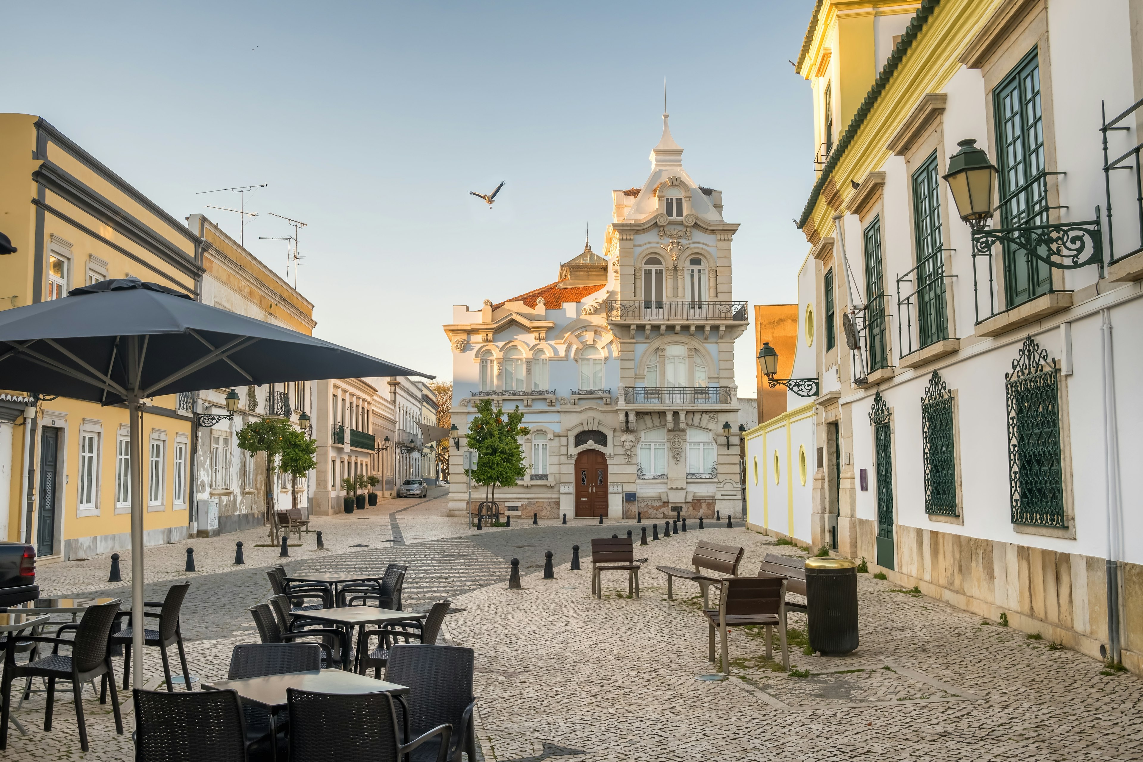 A beautiful 19th-century mansion on a square with tile pavements and outdoor tables, lined with other historic buildings