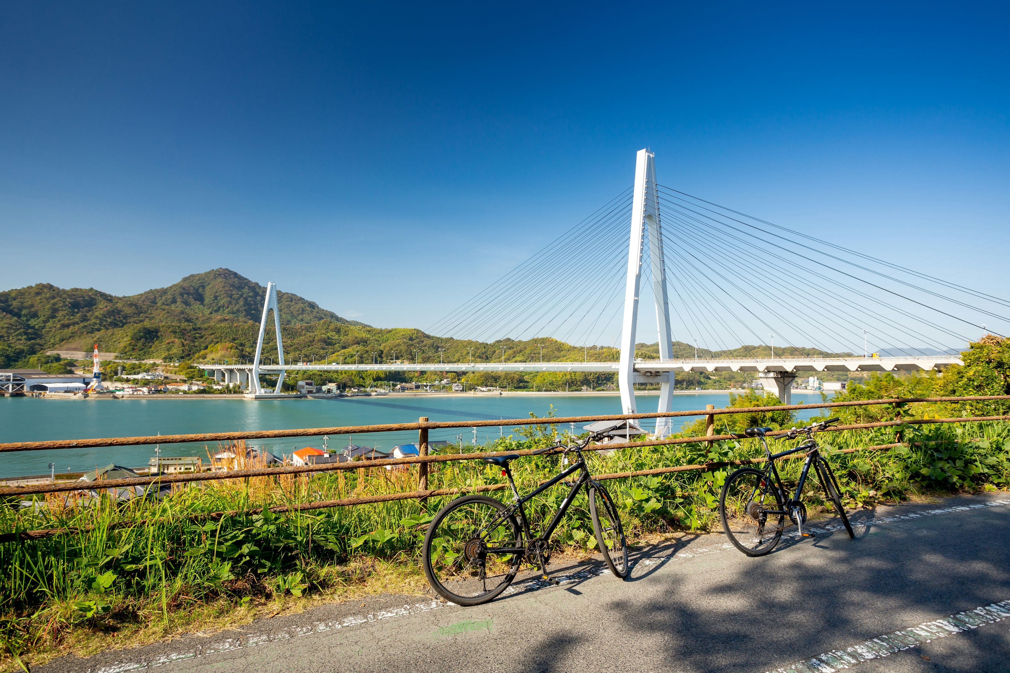 Two bicyles lean against railings near a large suspension bridge that links up two islands