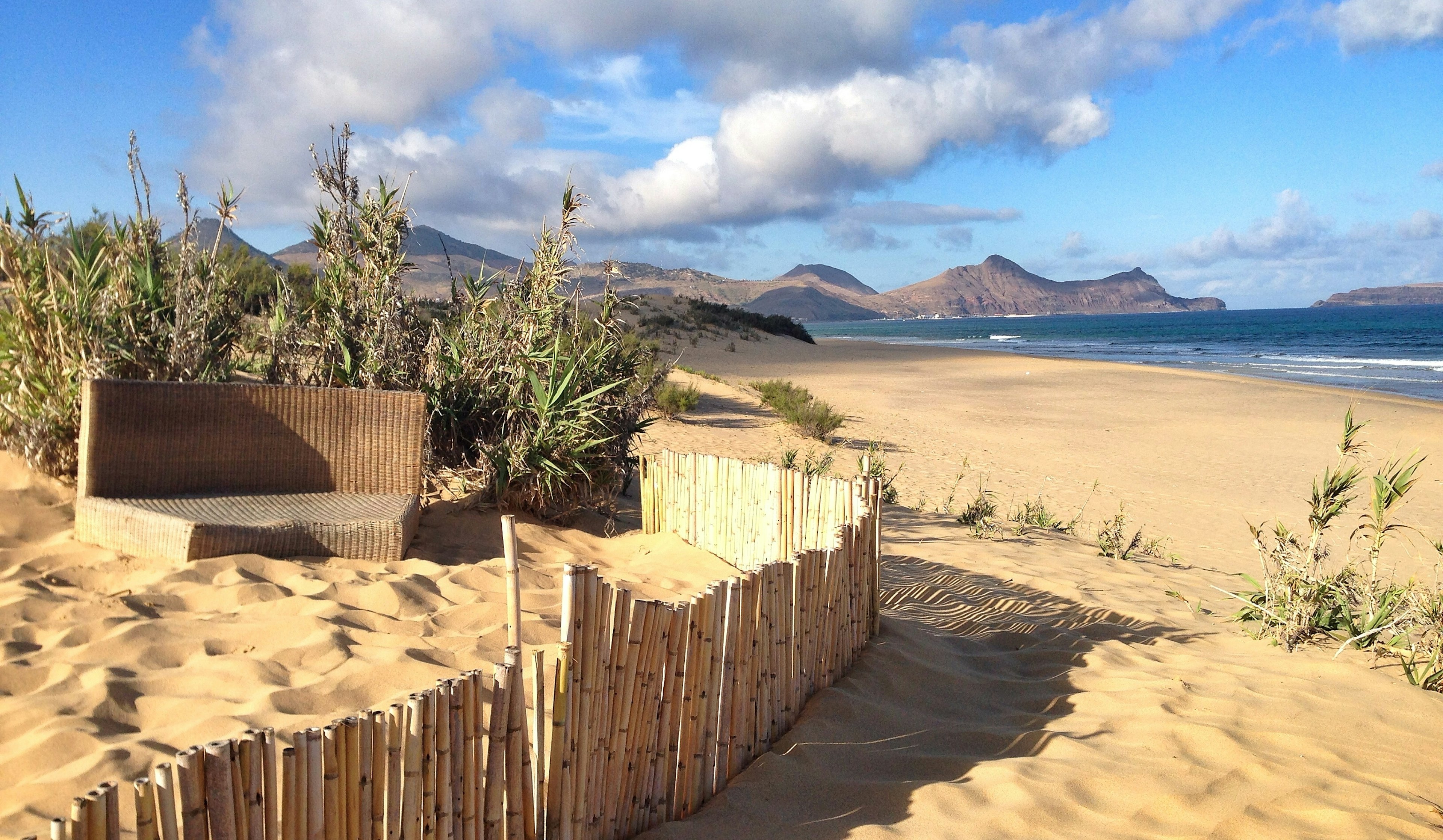 Deserted sandy beach of Porto Santo with a bambo seat and bamboo-fringed enclosure in forefront.