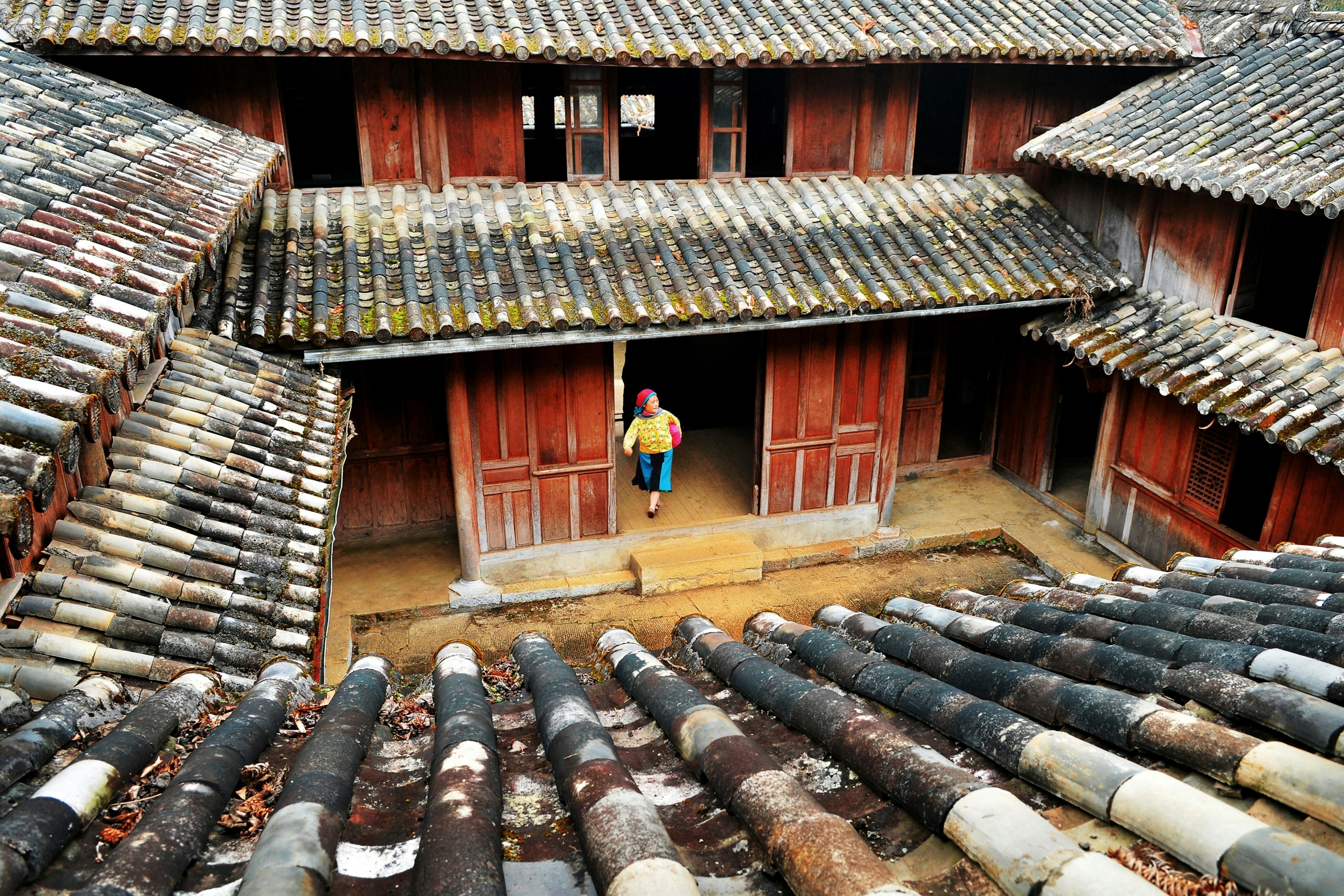 A woman in traditional clothing enters the courtyard of an elegant palace. The is from the roof, which is covered with cylindrical shingles