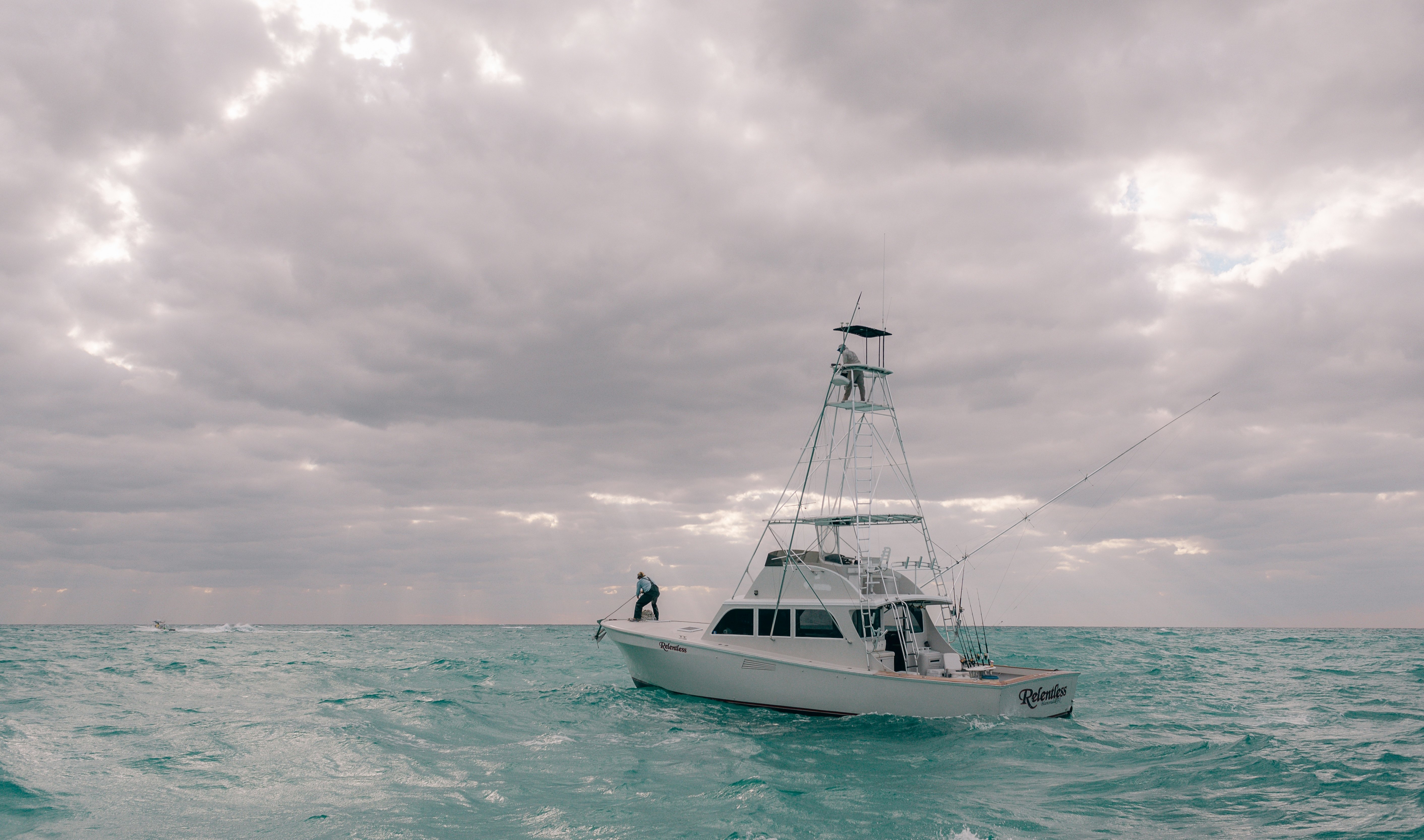 A sport-fishing boat takes to the blue waters of the open sea on an overcast day featuring thick gray clouds