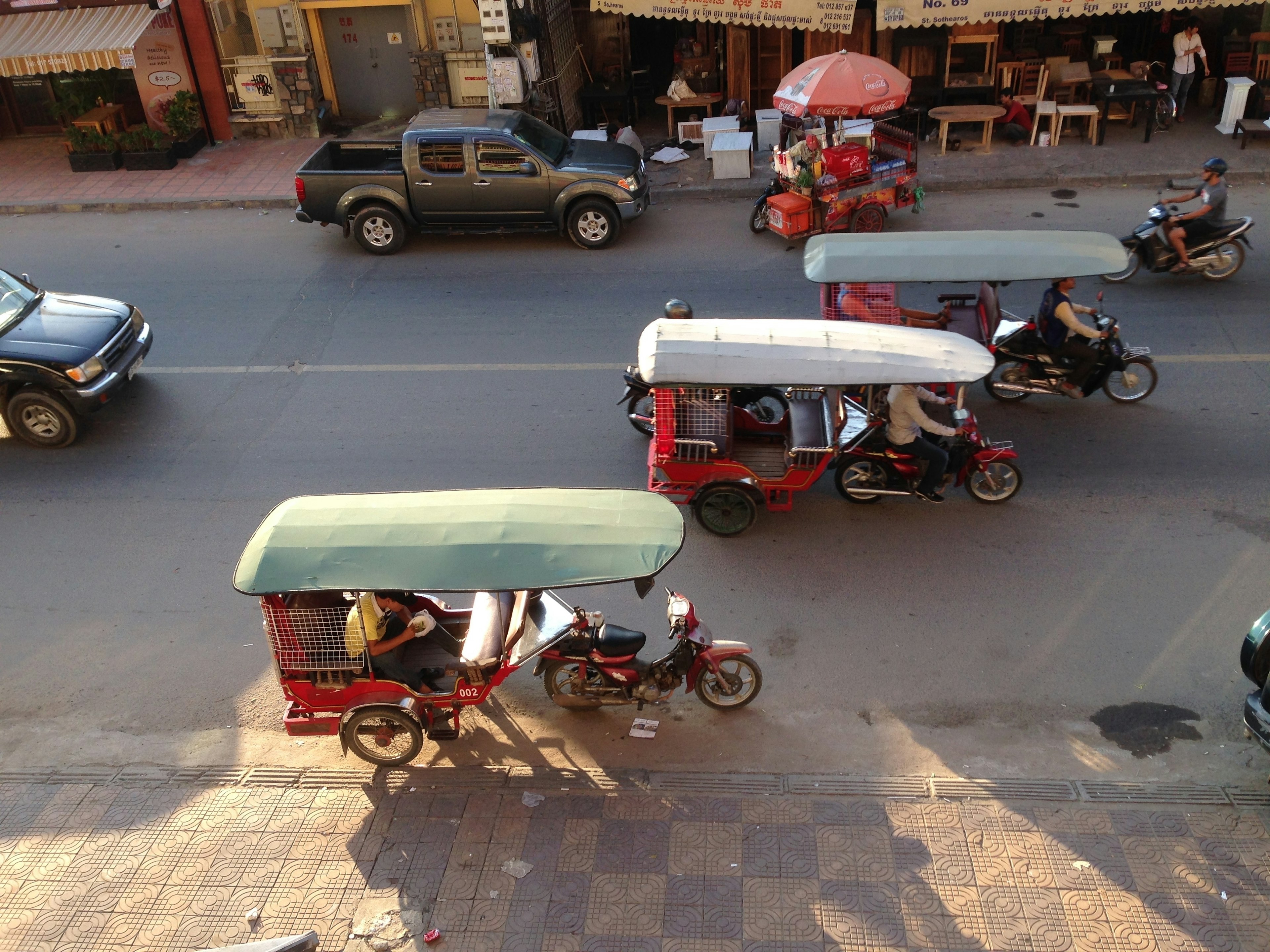 An overhead view of three tuk-tuks passing by on the road in the city street in the evening