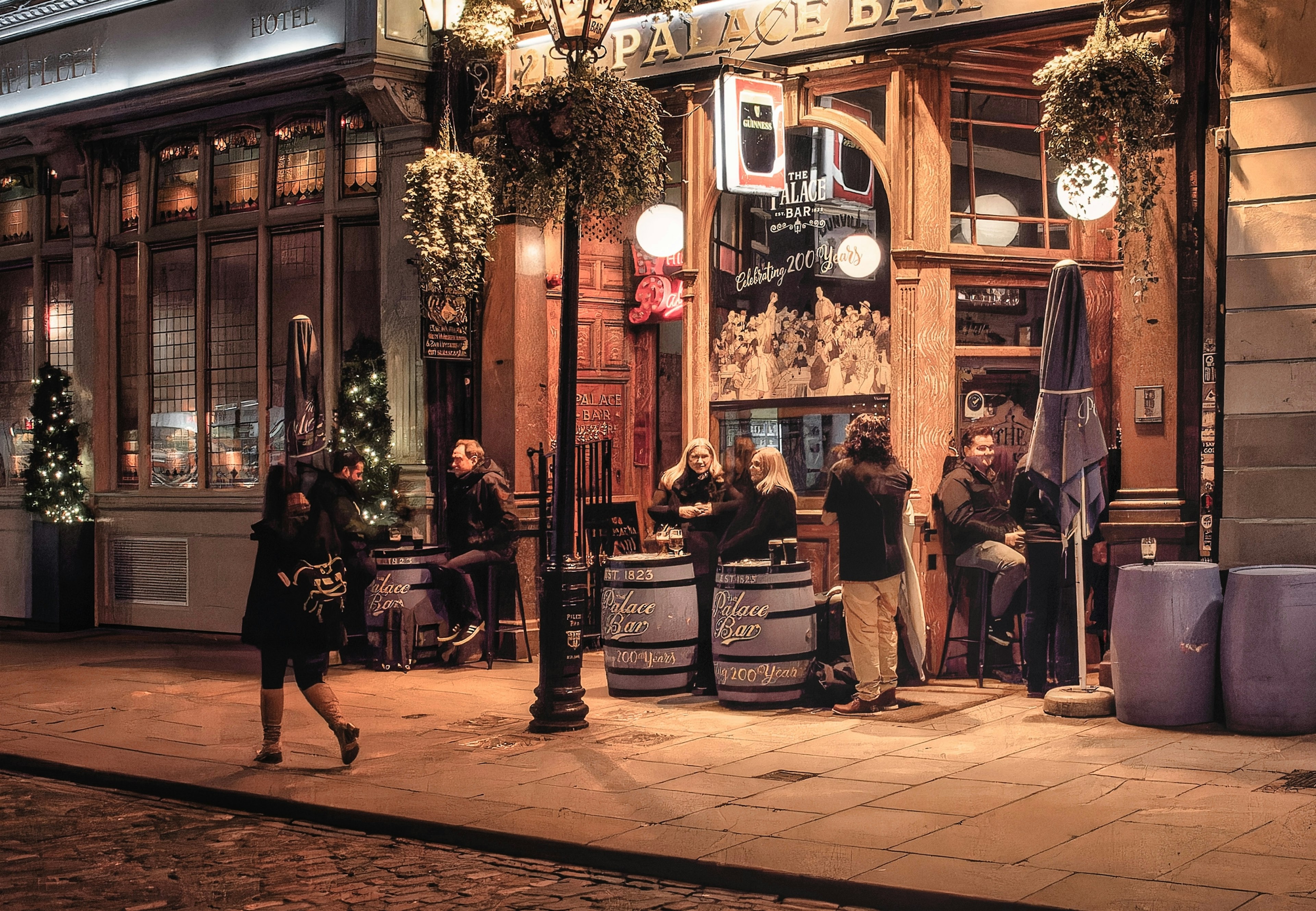 Exterior shot of The Palace Bar in Dublin at dusk with people sitting at beer barrels styled as outdoor tables.