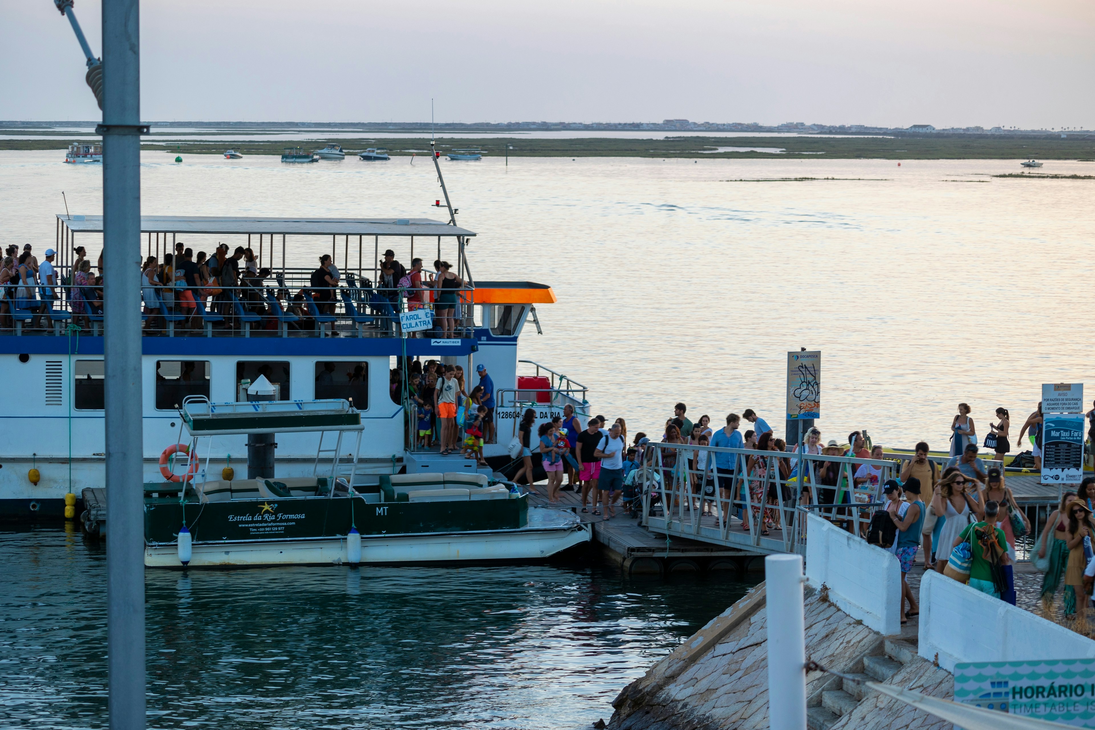 Numerous passengers disembark from a ferry and onto a pier